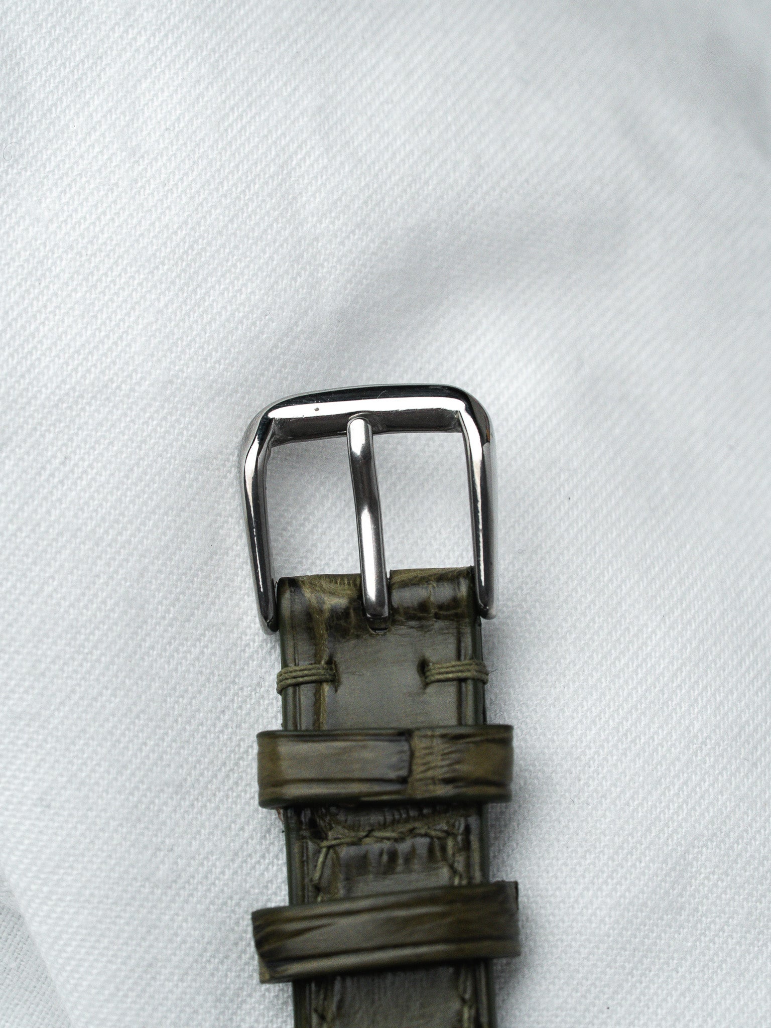 Vintage watch strap with olive green alligator texture and polished steel buckle on white fabric