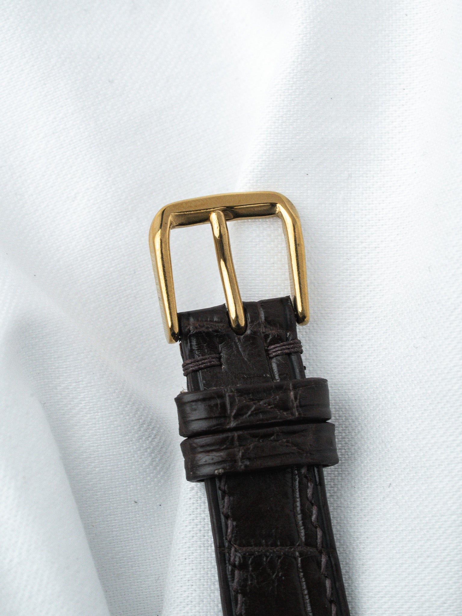 Vintage watch strap with dark brown alligator leather and gold buckle on white fabric