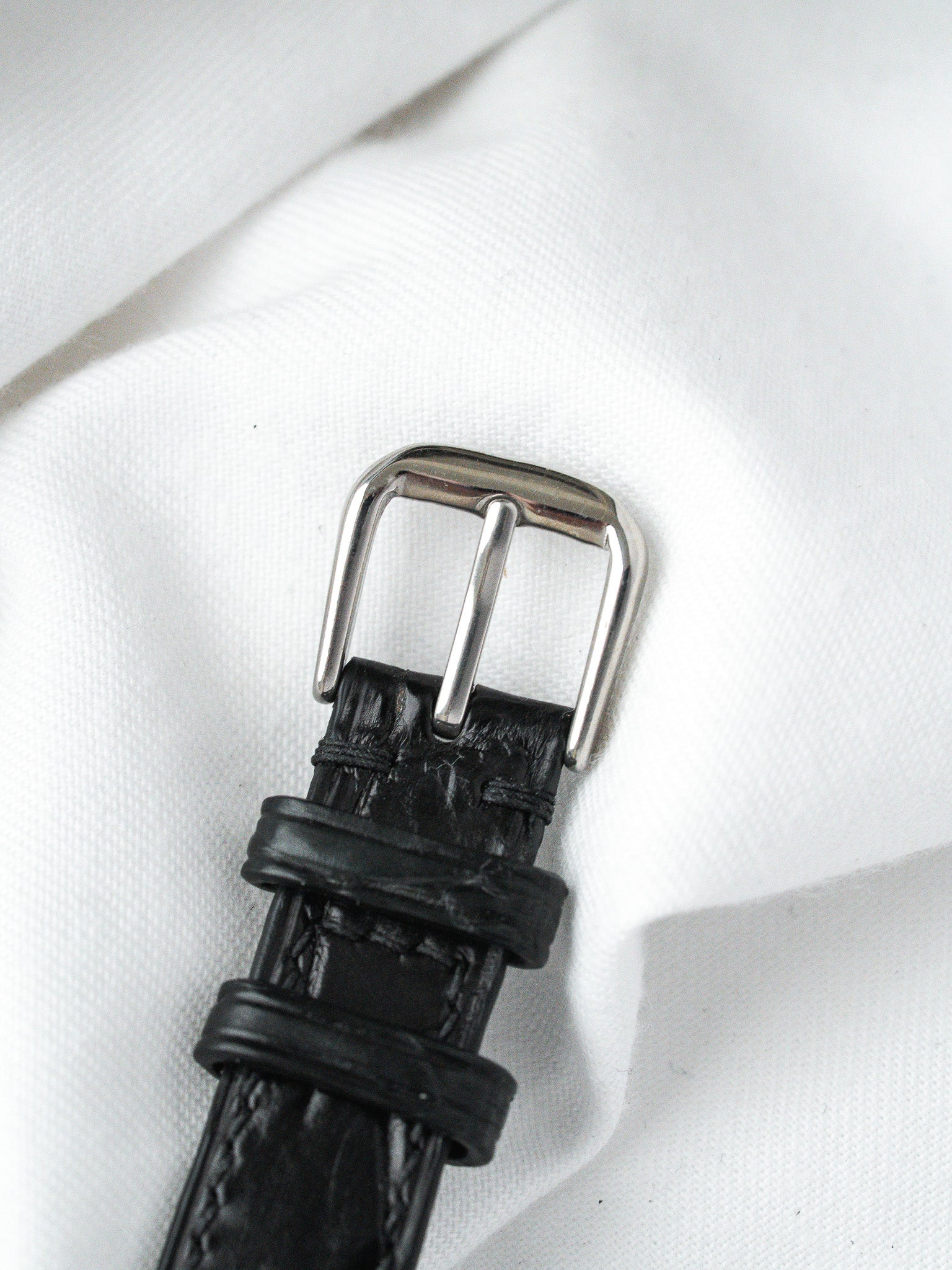 Black leather watch strap with silver buckle on white fabric
