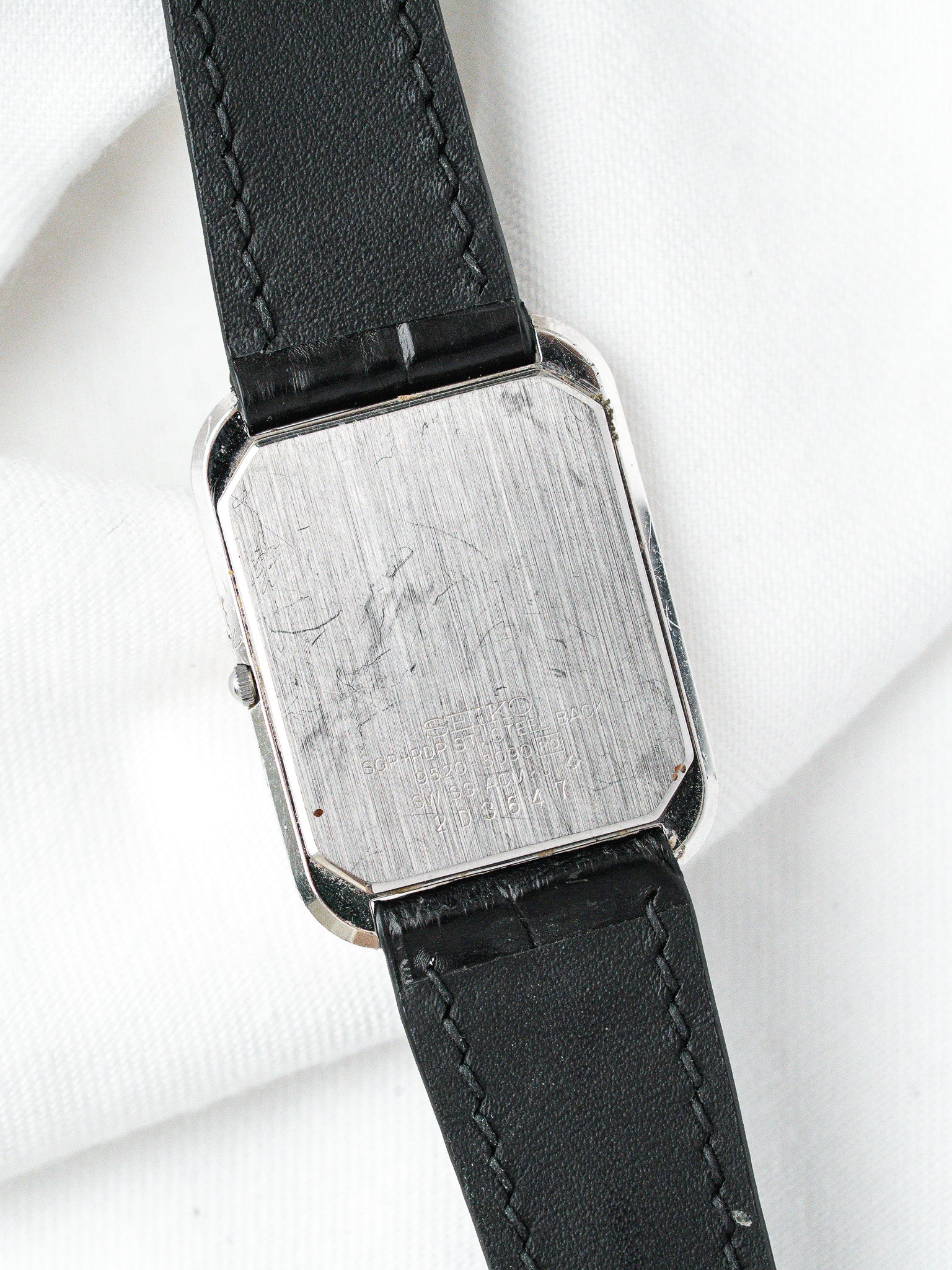 Seiko vintage watch with steel case, black leather strap, back view on white