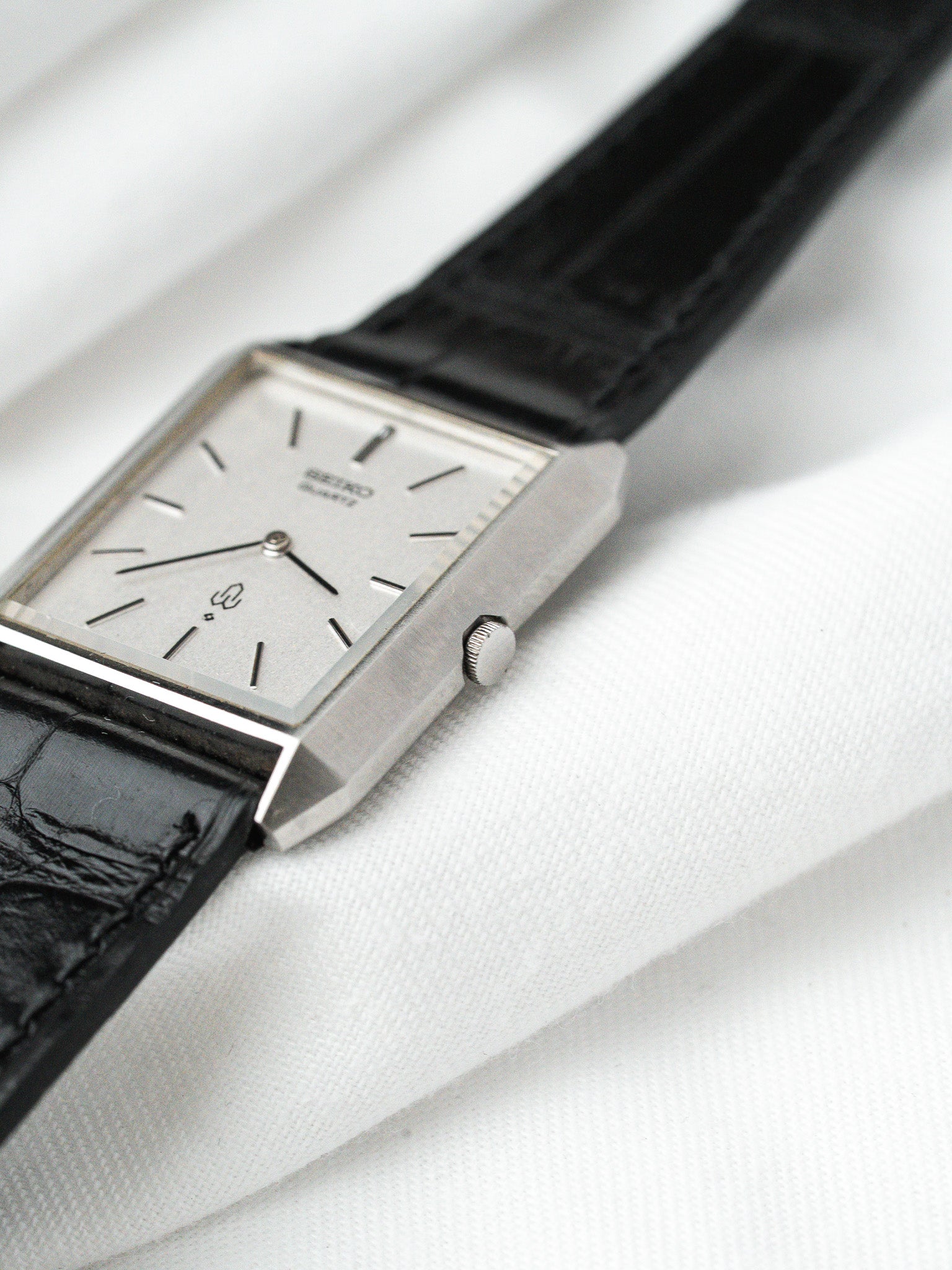 Seiko vintage watch with silver dial, black leather strap, rectangular case on white fabric