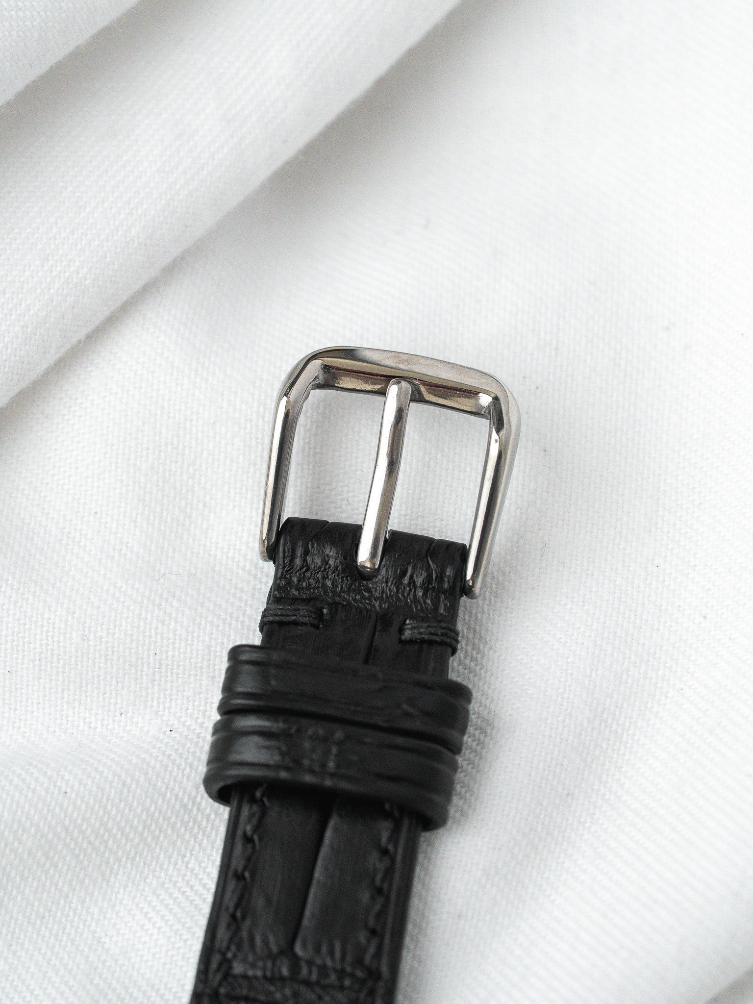 Black leather watch strap with textured pattern and silver buckle on white fabric