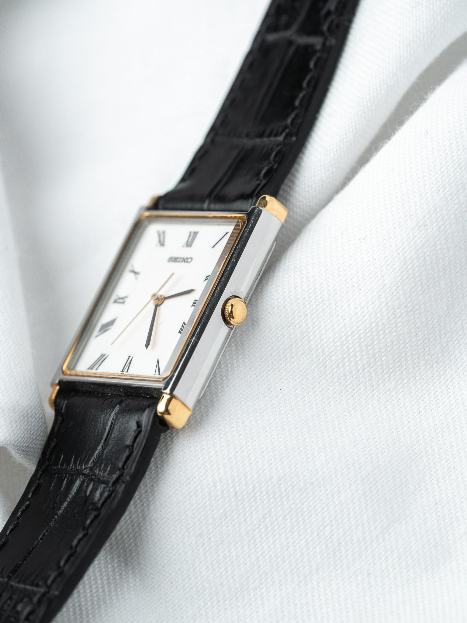 Seiko vintage watch with white dial, Roman numerals, gold accents, black leather strap on white fabric