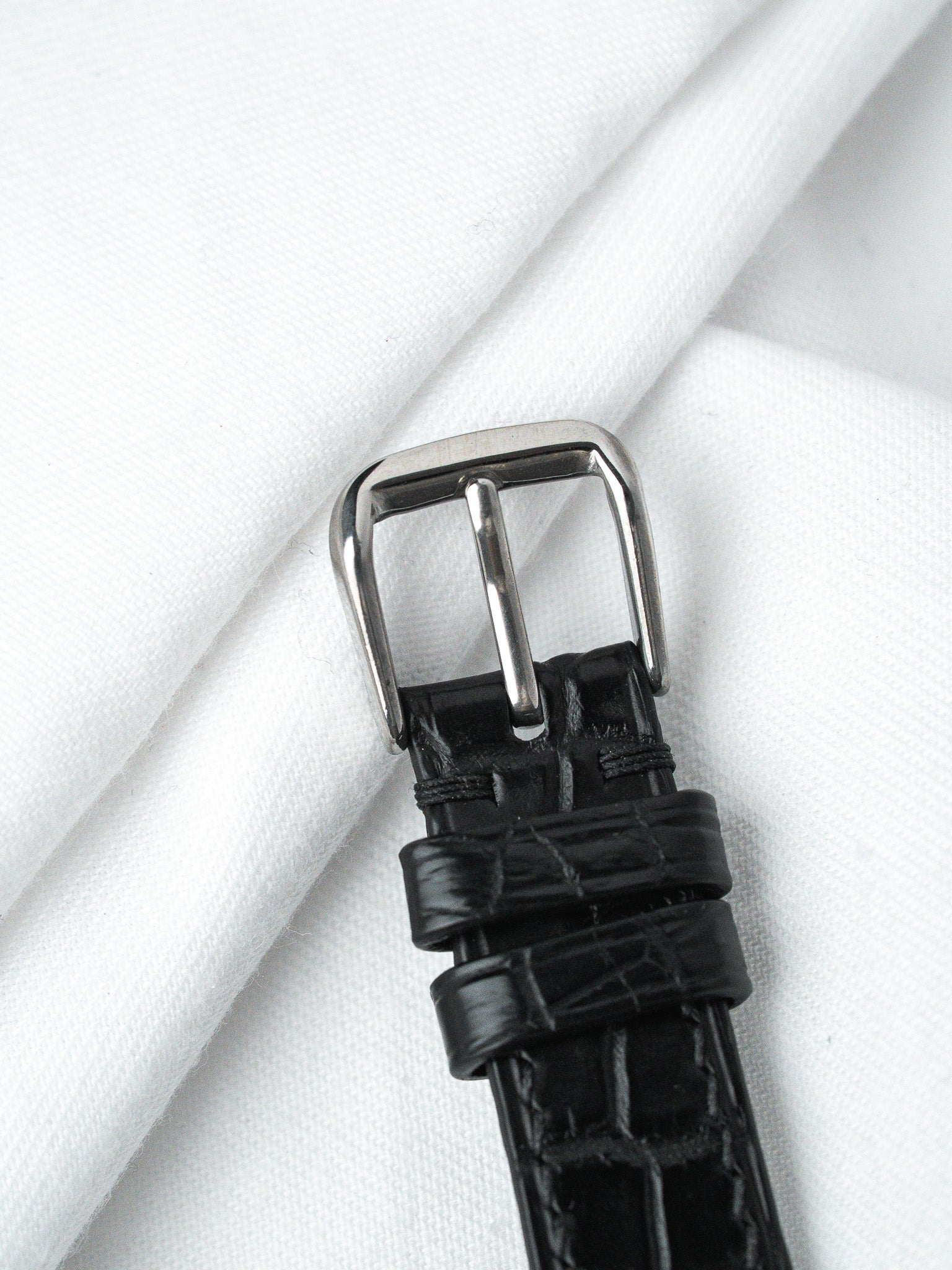 Black alligator leather watch strap with polished steel buckle on white fabric