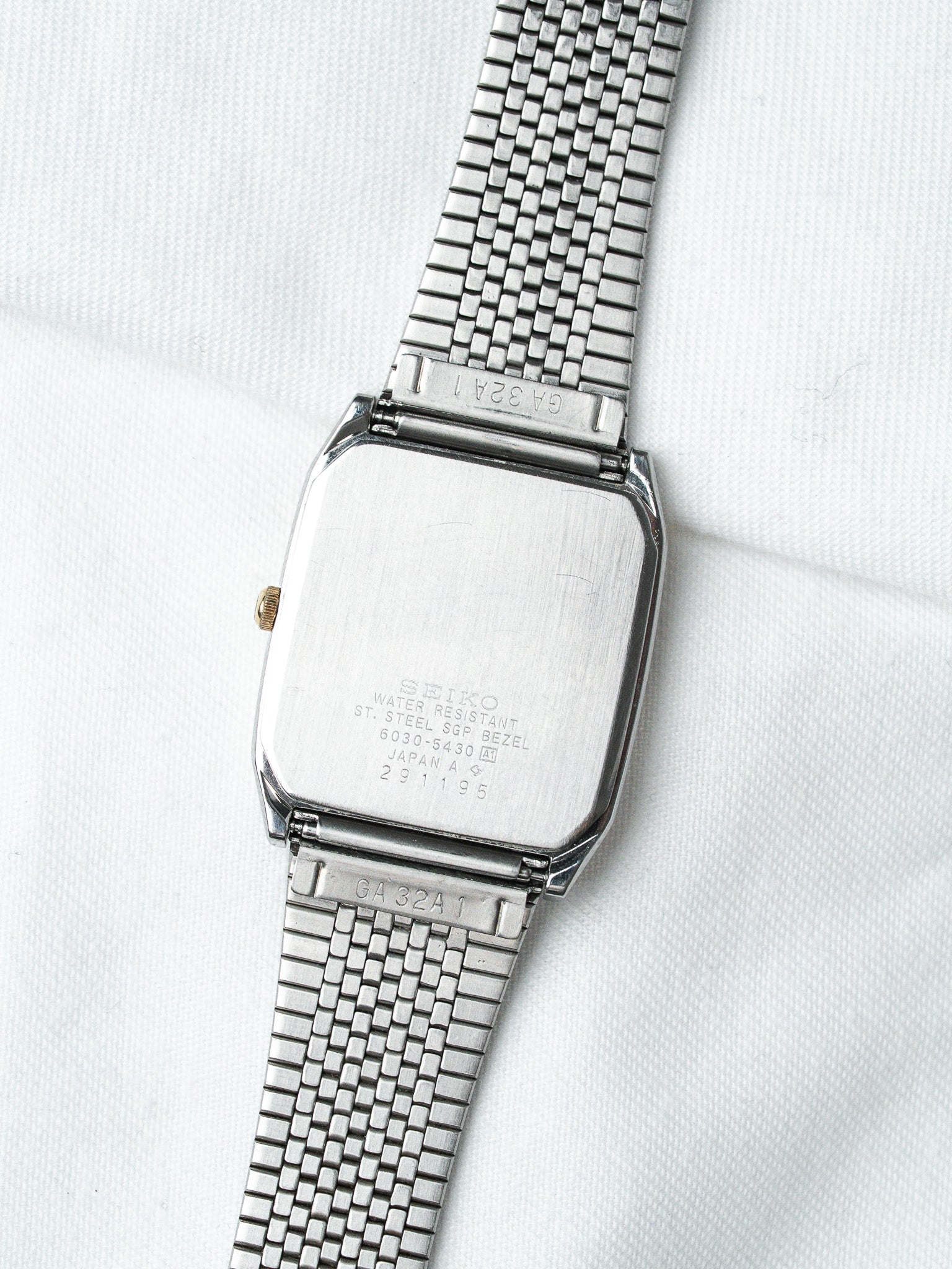 Seiko vintage watch with stainless steel case and mesh bracelet, back view on white fabric