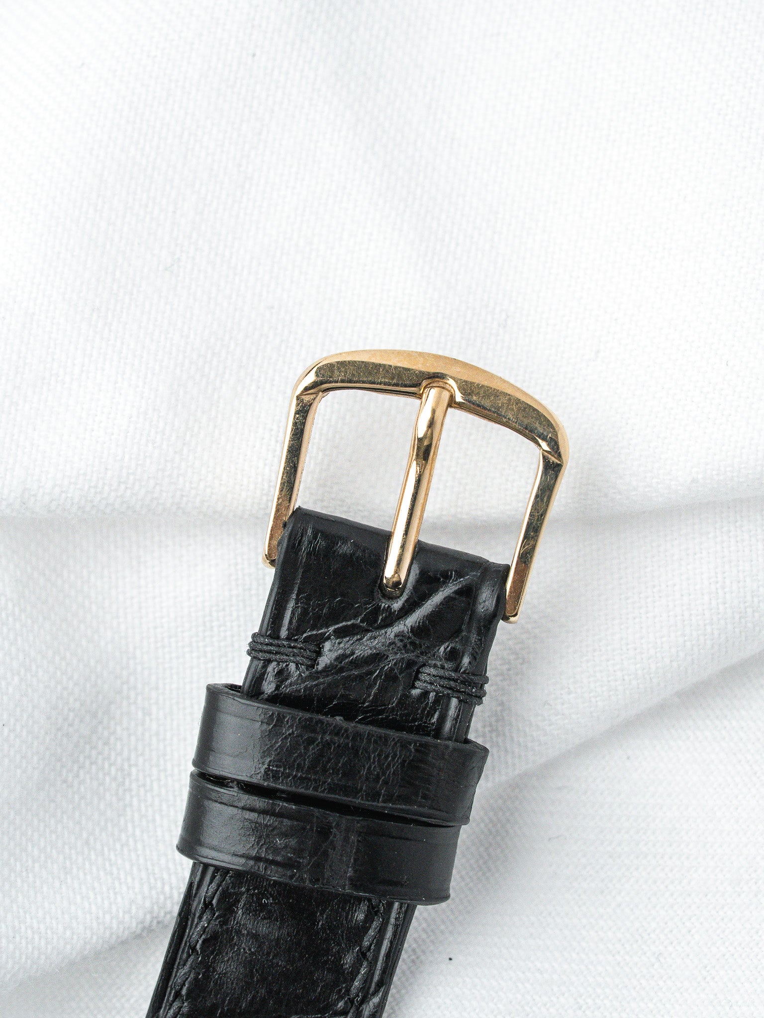 Black alligator leather watch strap with gold buckle on white fabric