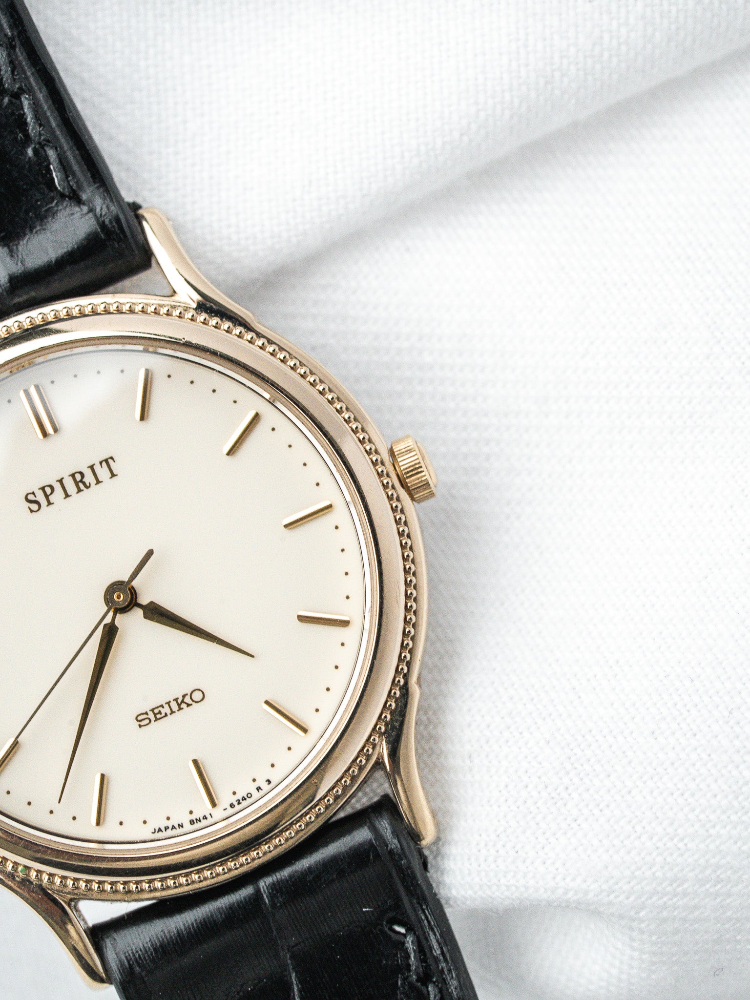 Seiko Spirit vintage watch with gold case, white dial, black leather strap on white fabric