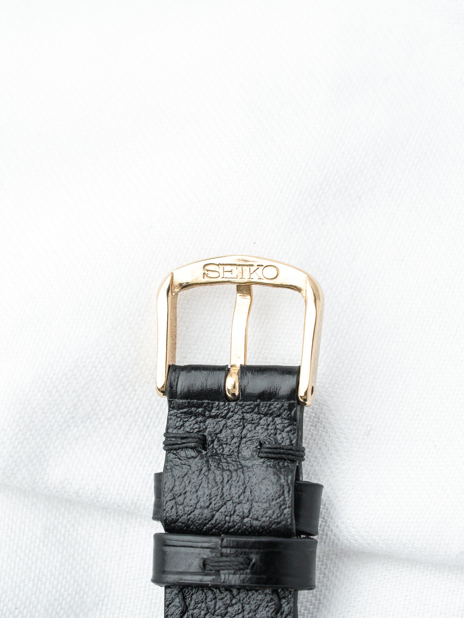 Seiko watch buckle with gold tone clasp and black textured leather strap
