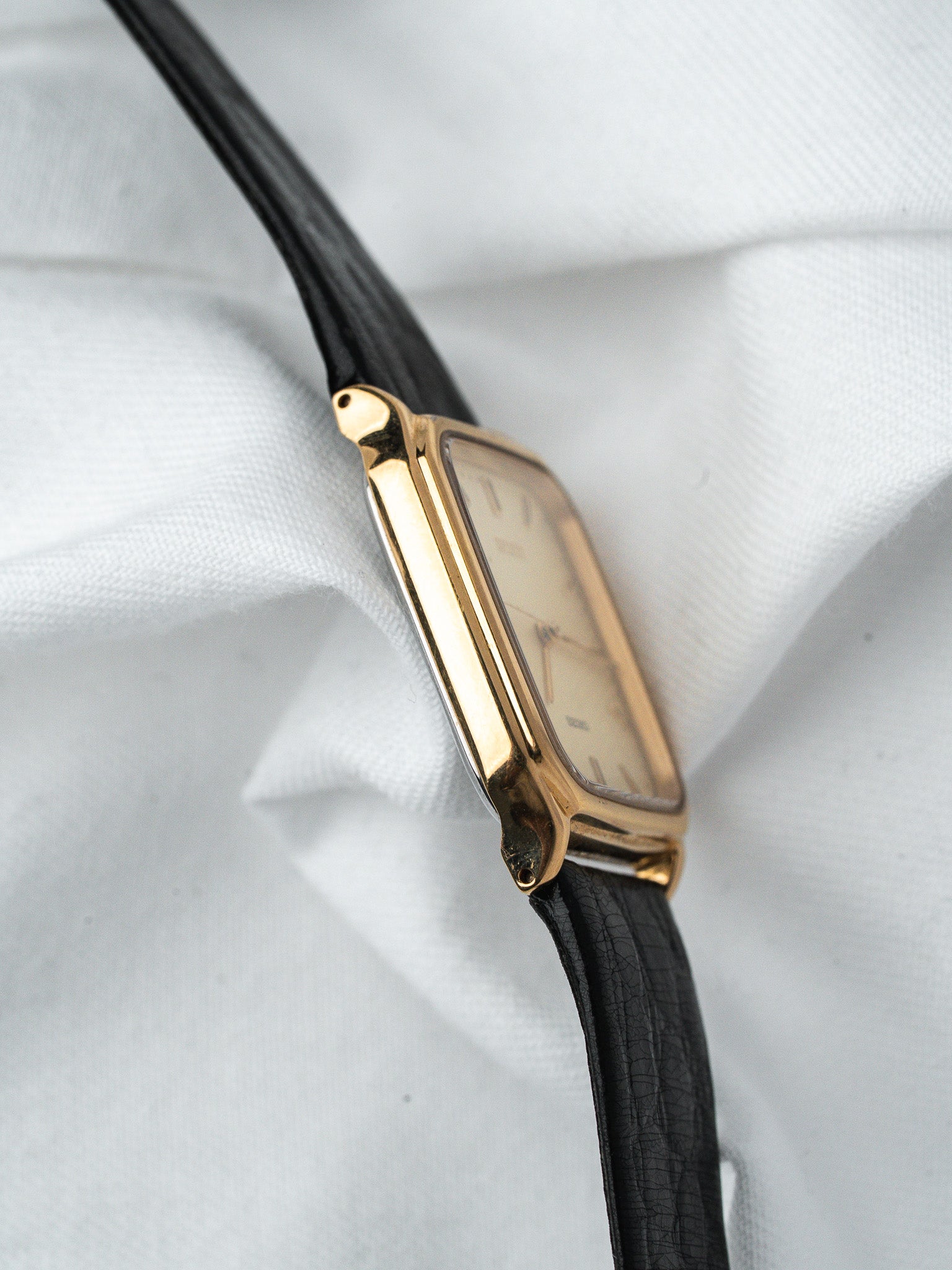 Cartier vintage watch with gold case, cream dial, black leather strap on white fabric