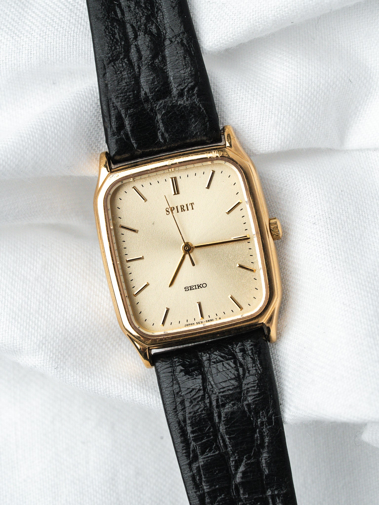Seiko Spirit vintage watch with gold case, cream dial, black textured strap on white fabric