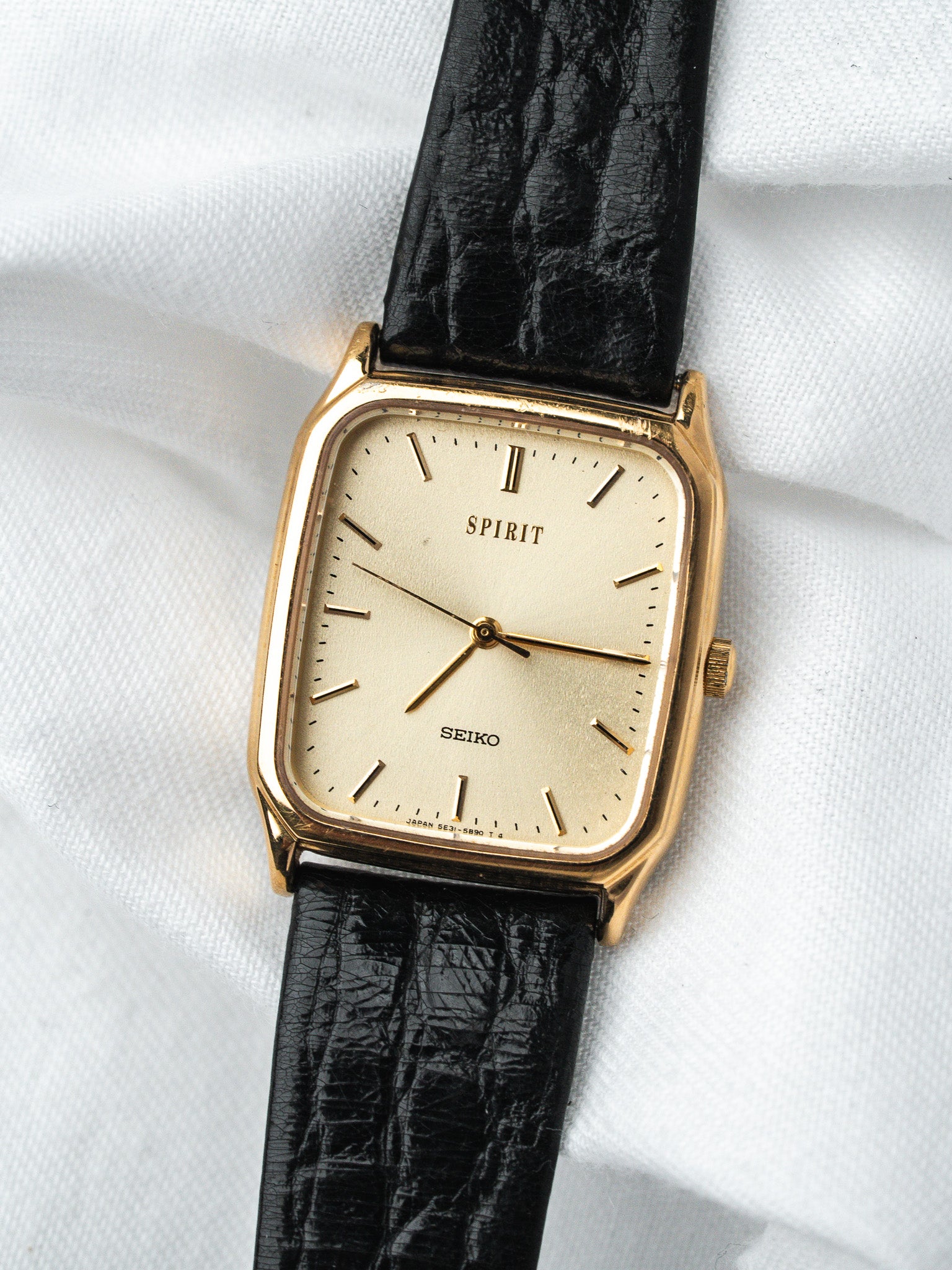 Seiko Spirit vintage watch with gold case, cream dial, black leather strap on white fabric