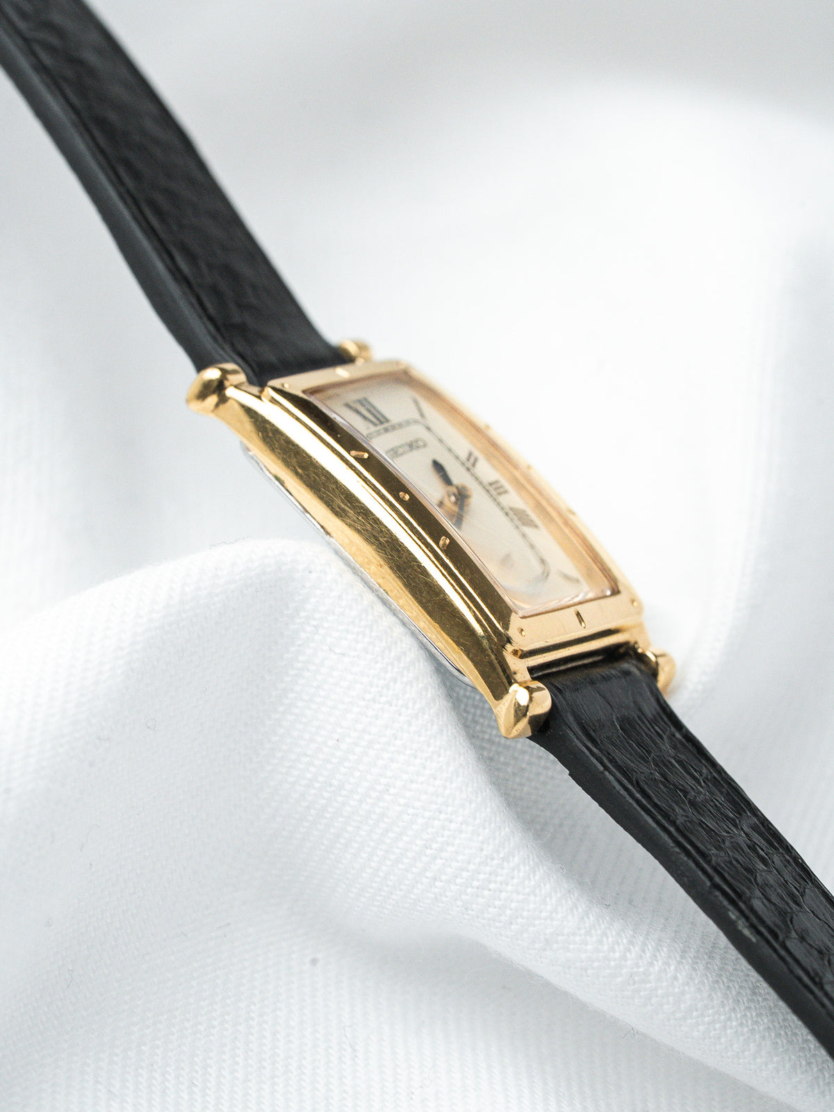 Cartier Tank vintage watch with gold case, white dial, black leather strap on white fabric