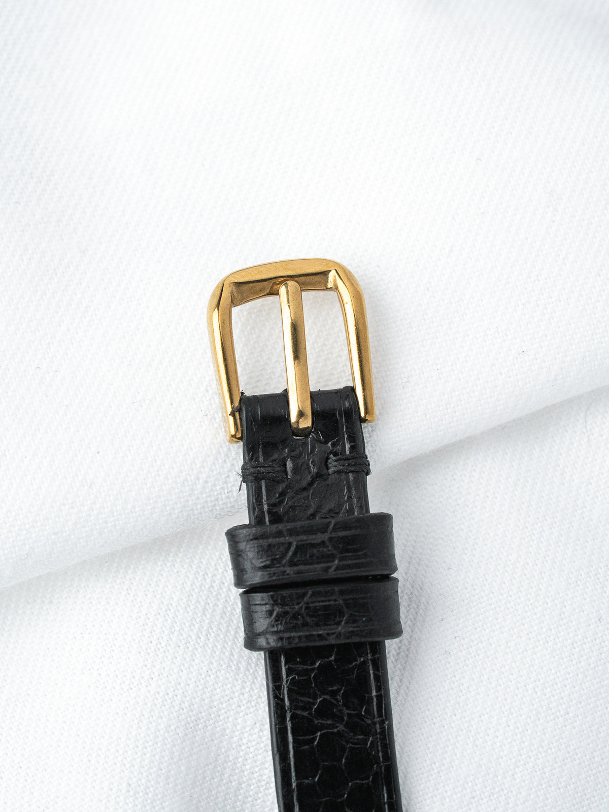 Black alligator leather watch strap with gold buckle on white fabric