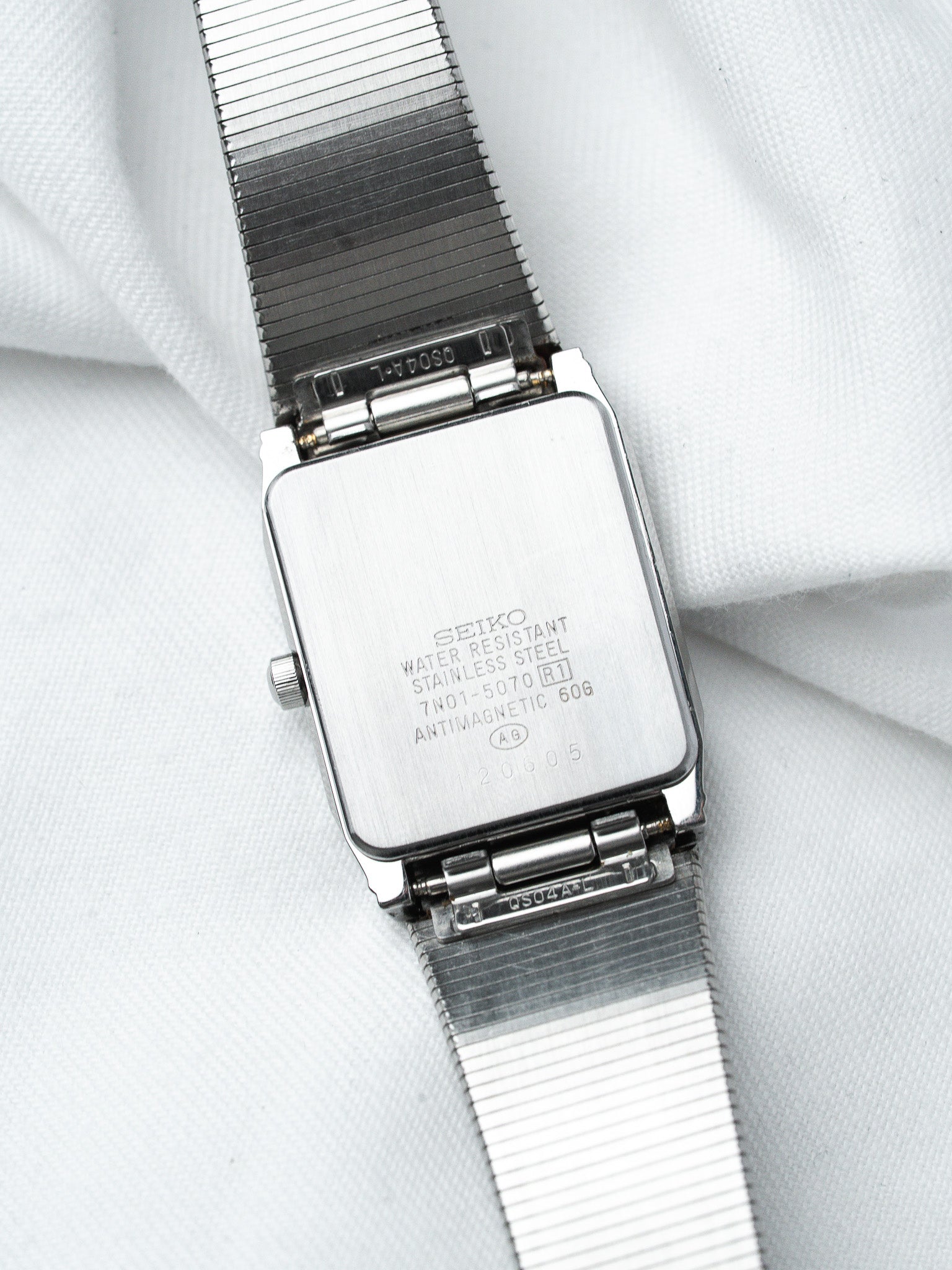 Seiko vintage watch back, stainless steel case with engraved specs, mesh bracelet on white fabric