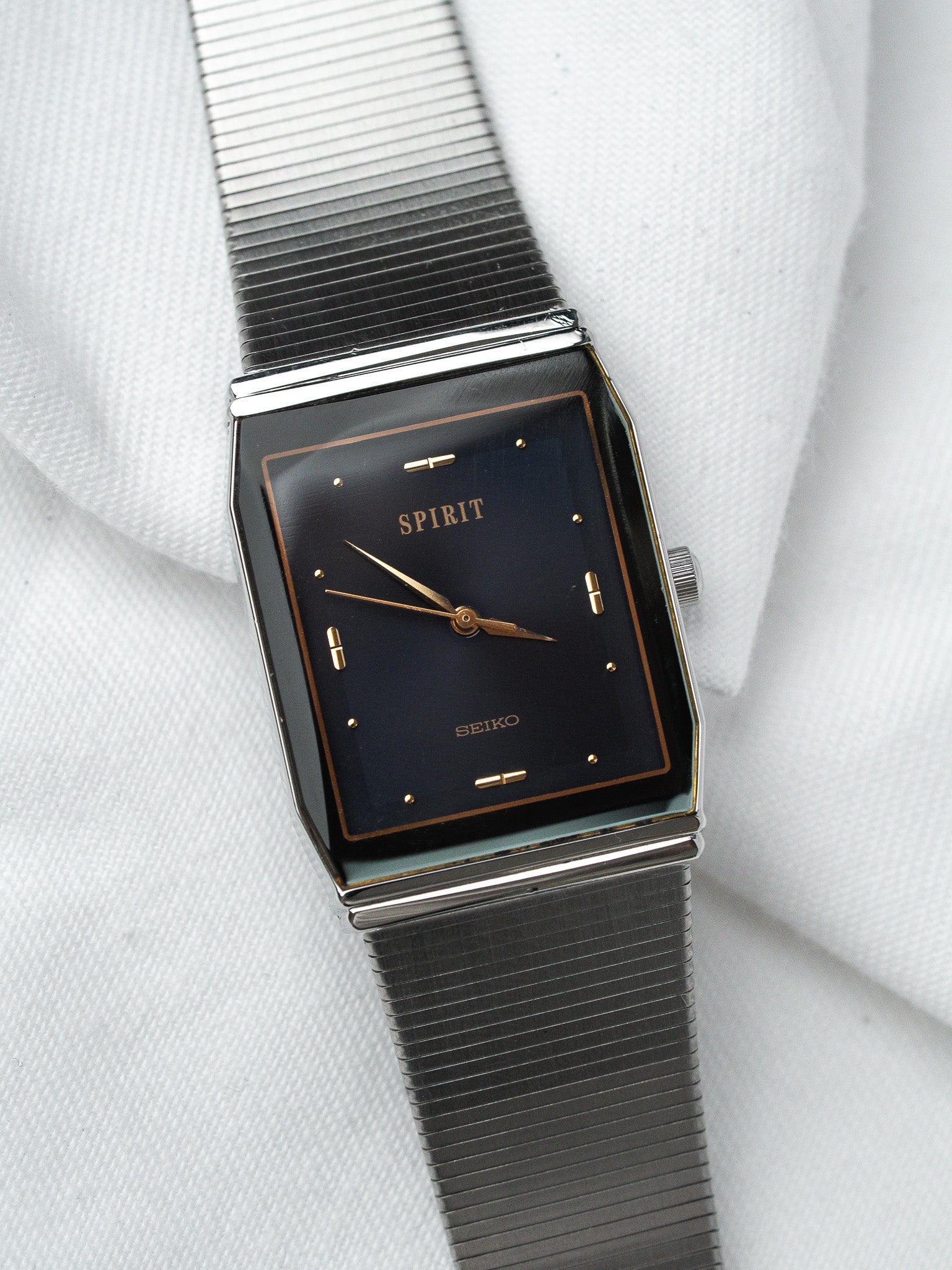 Seiko Spirit vintage watch with black dial, gold markers, and mesh bracelet on white fabric