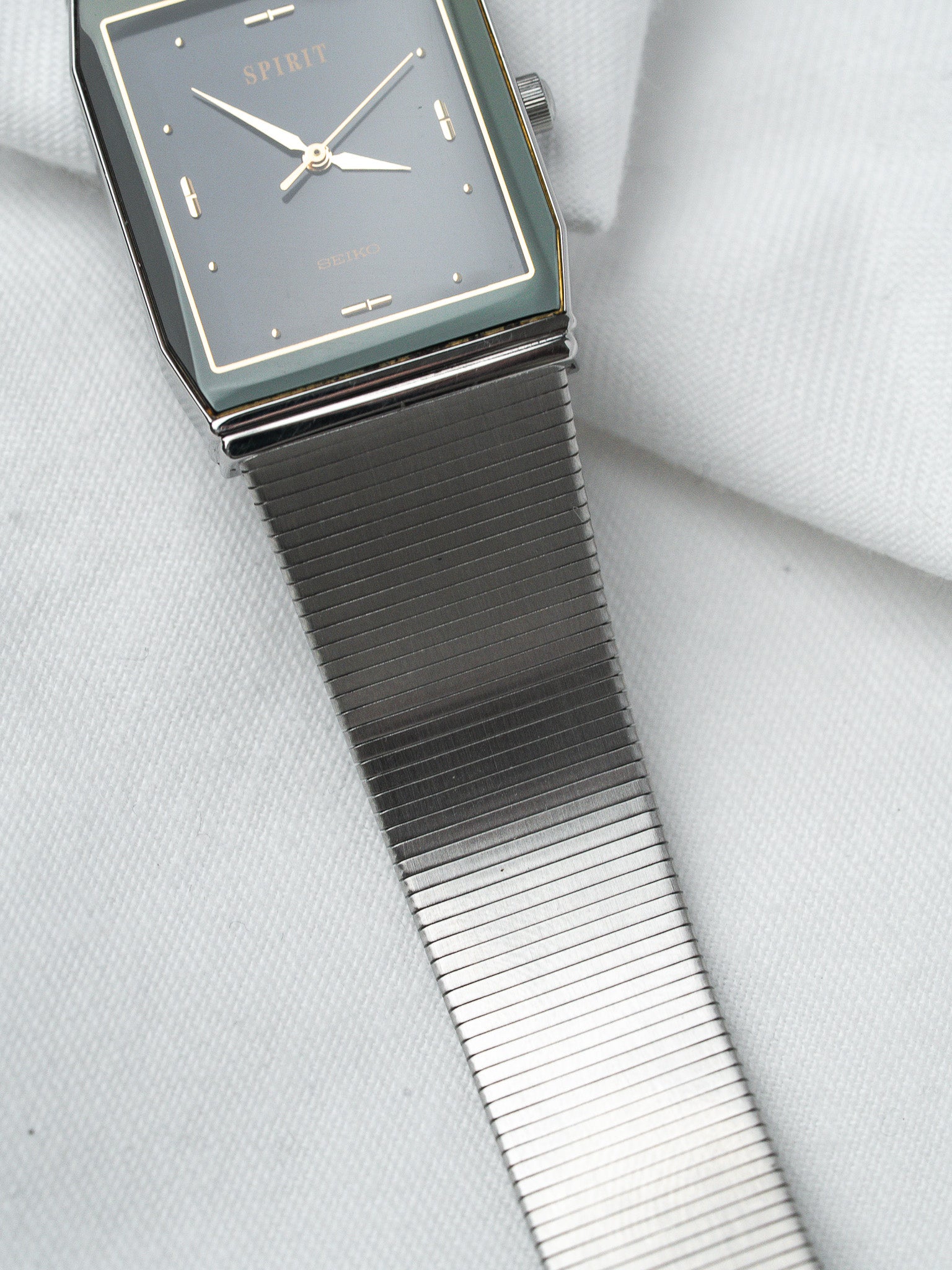 Seiko Spirit vintage watch with grey dial, gold markers, and mesh bracelet on white fabric