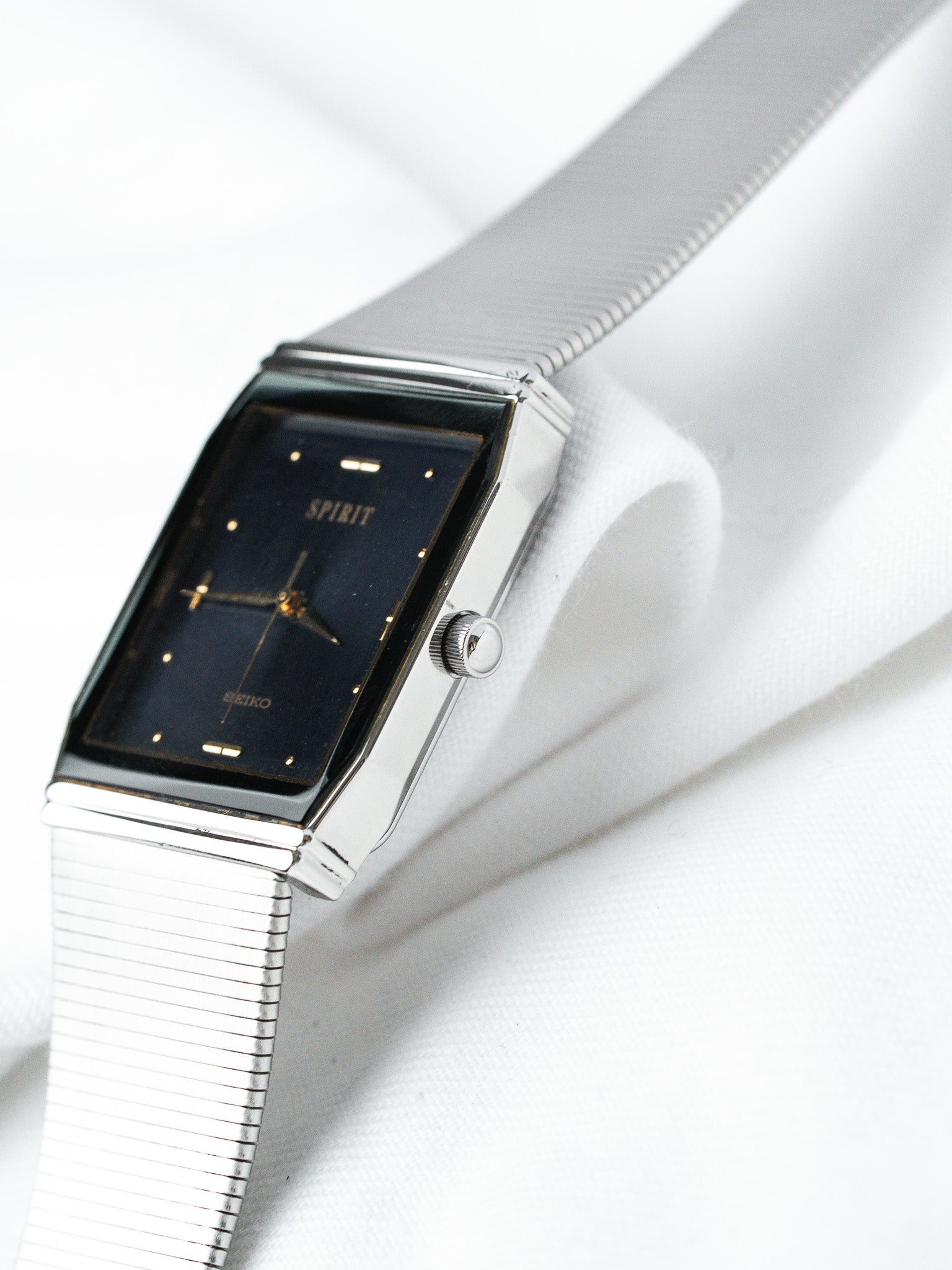 Seiko Spirit vintage watch with black dial, gold markers, and silver mesh bracelet on white fabric