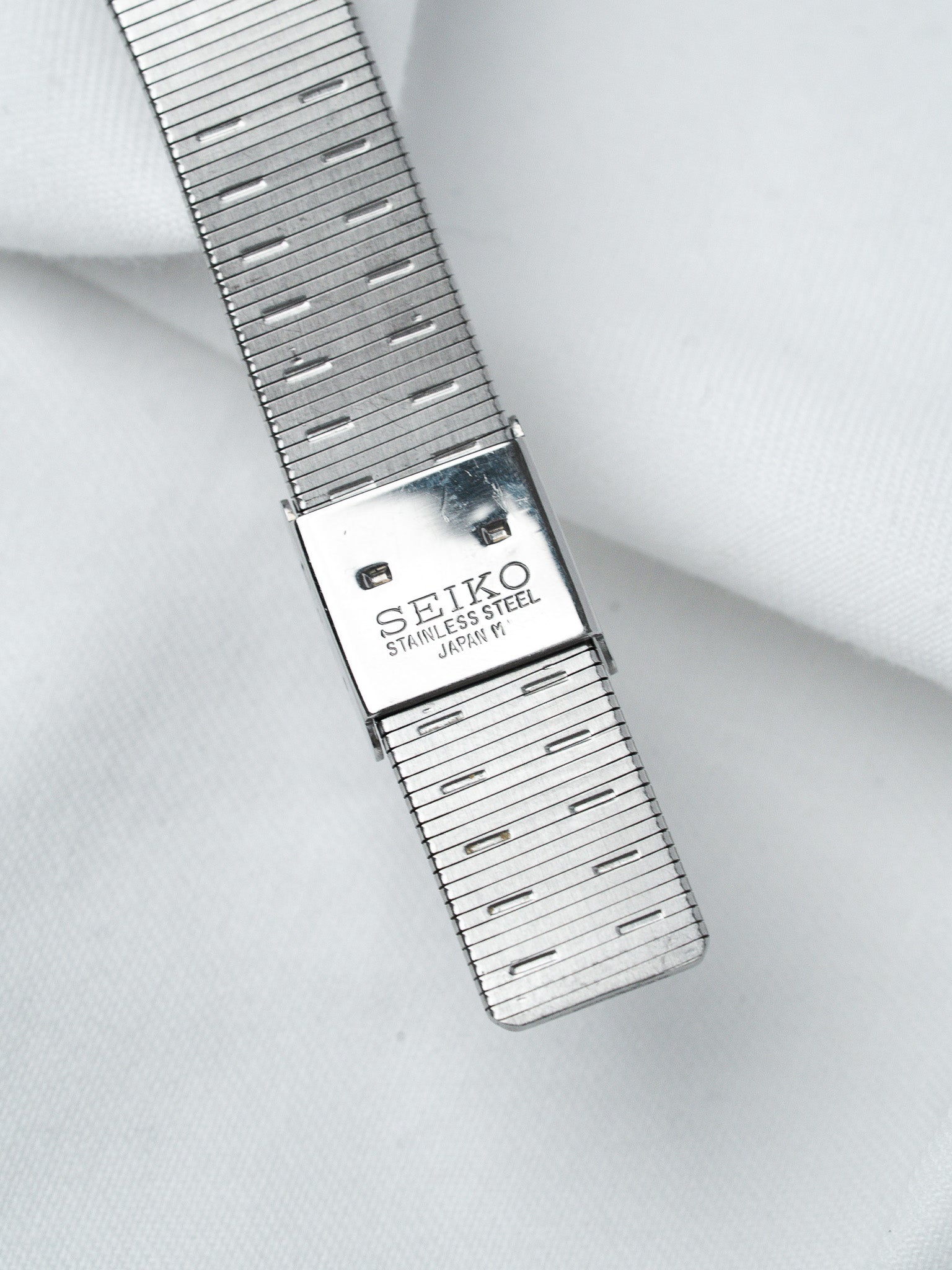 Seiko stainless steel vintage watch bracelet with engraved clasp on white fabric