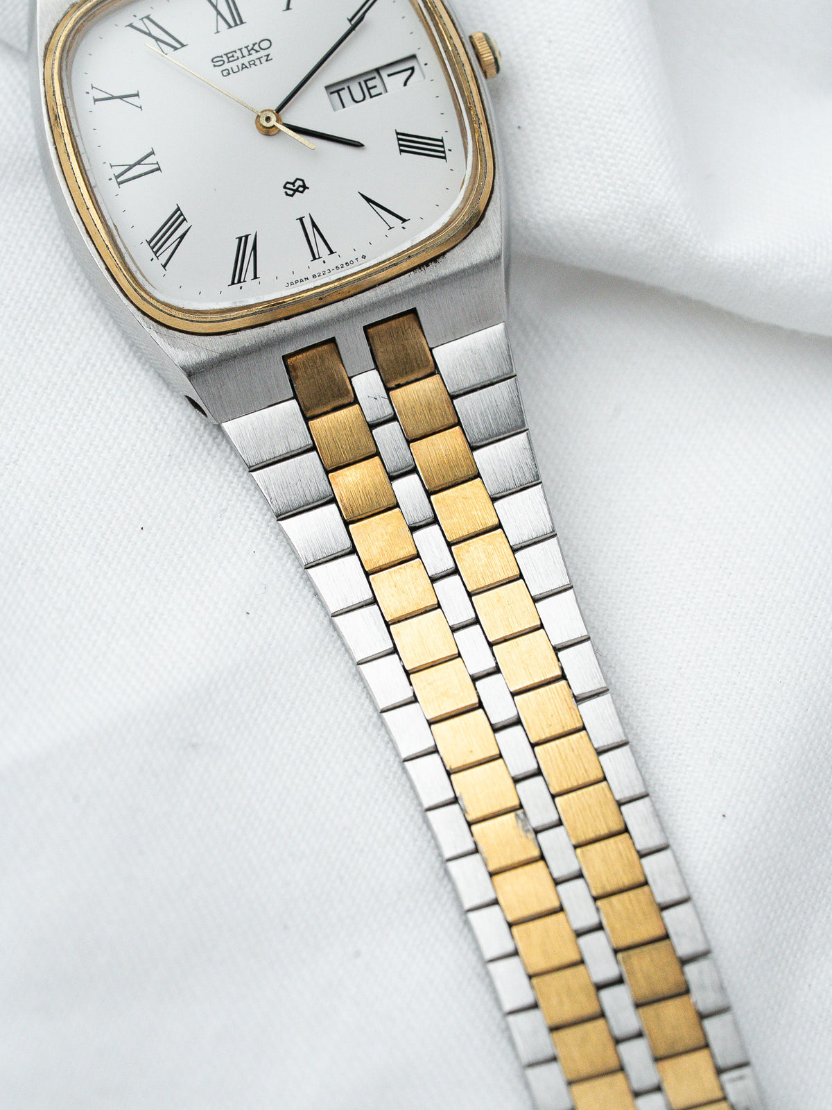 Seiko Quartz vintage watch with white dial, Roman numerals, two-tone bracelet on white fabric