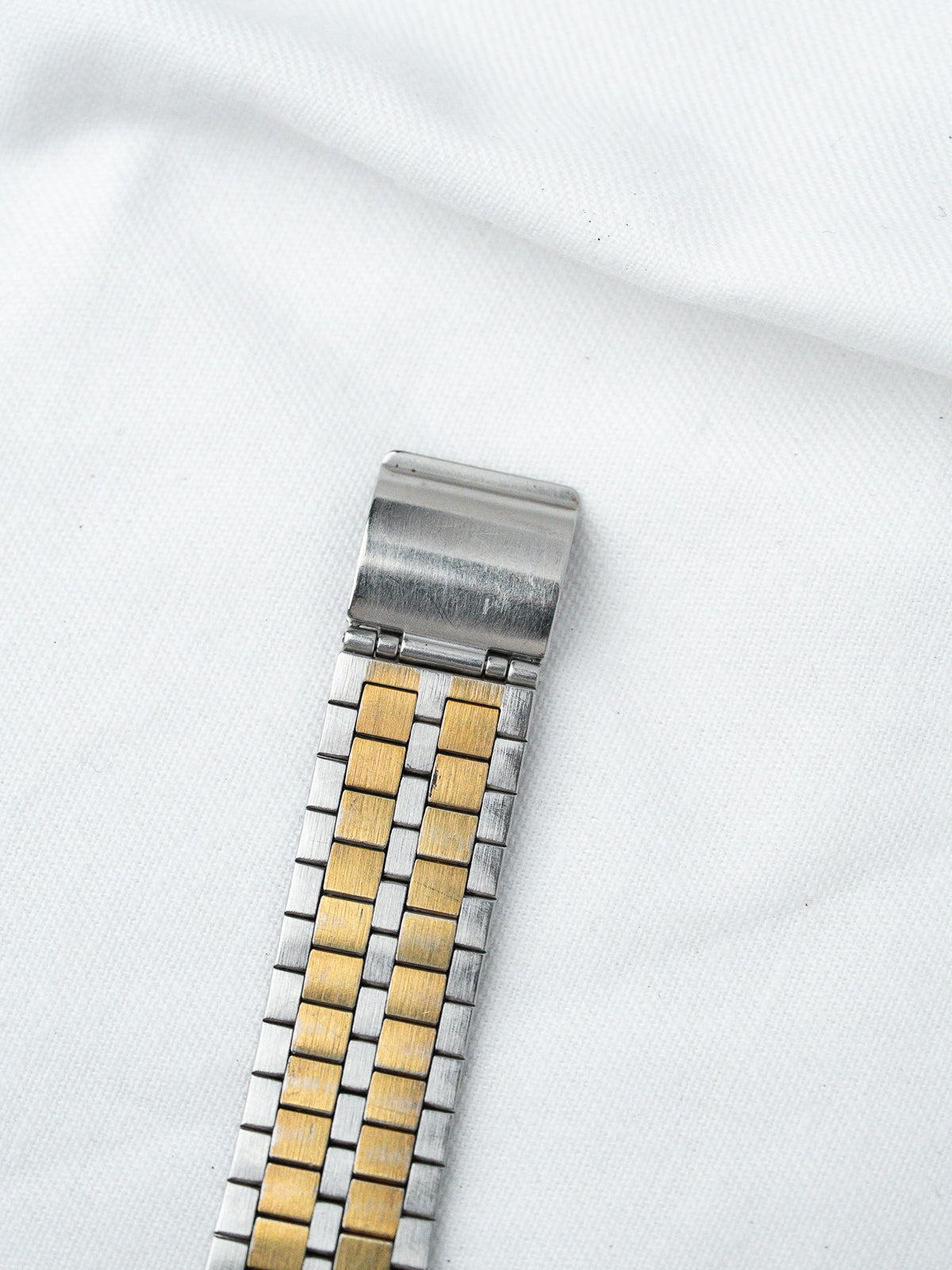 Vintage two-tone steel and gold watch bracelet on white fabric background