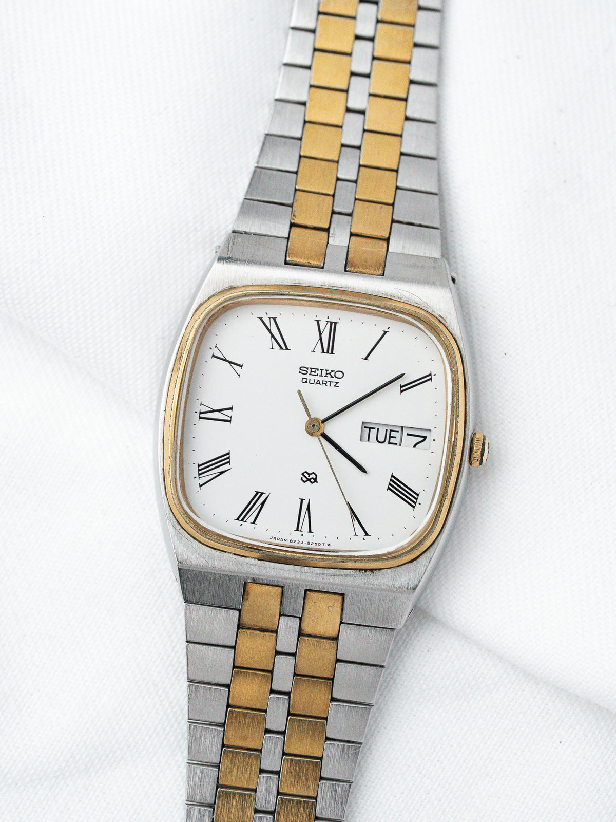 Seiko Quartz vintage watch with white dial, Roman numerals, gold and steel bracelet on white background