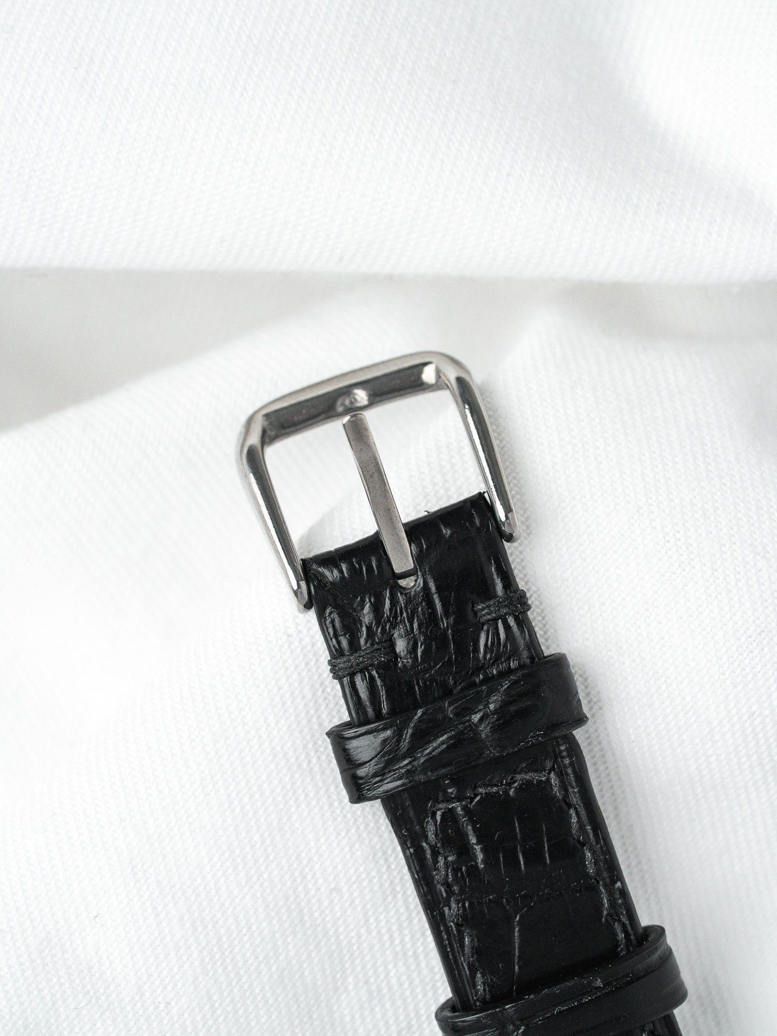 Black alligator leather watch strap with polished steel buckle on white fabric