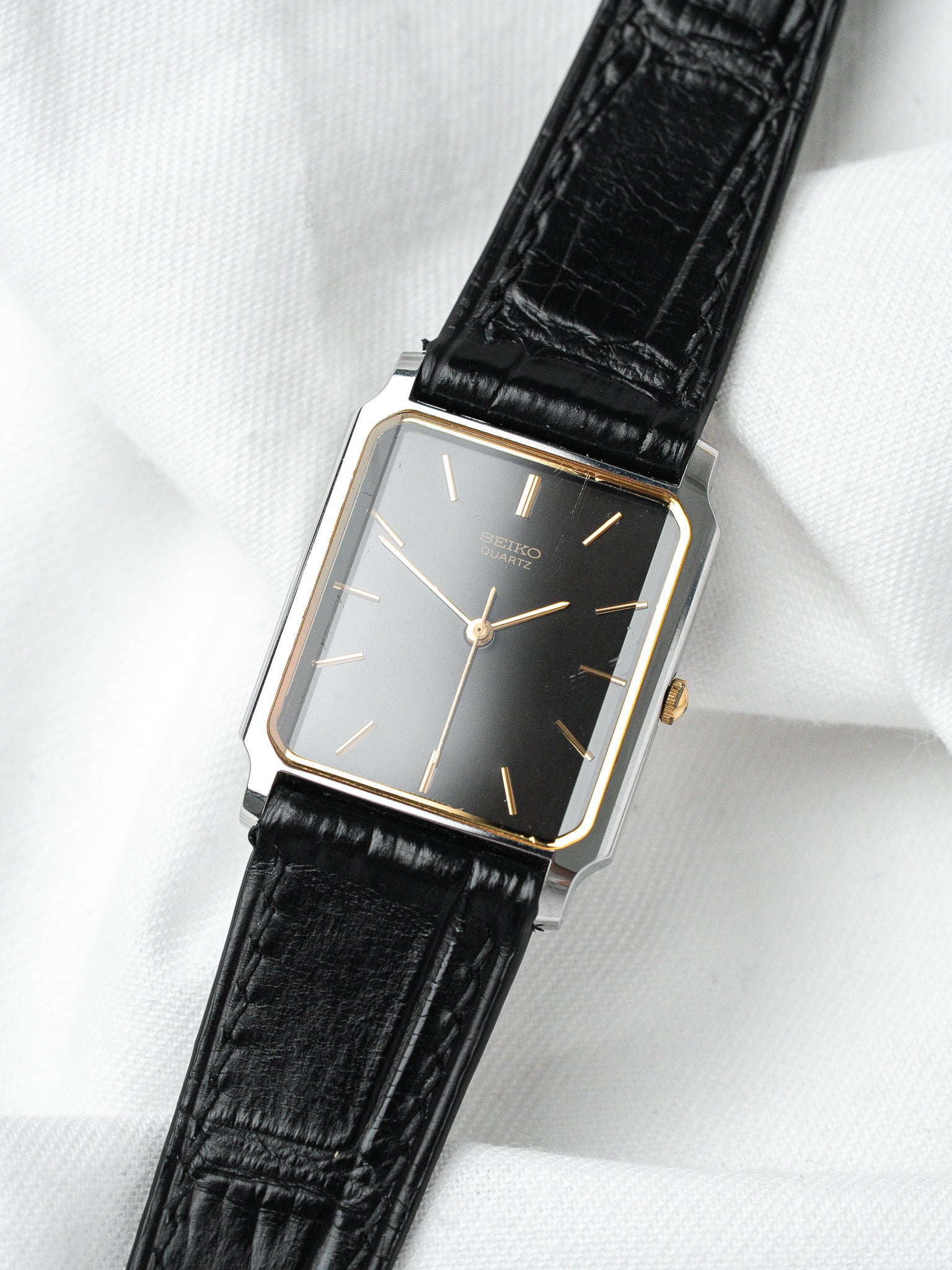 Seiko Quartz vintage watch with black dial, gold accents, and black leather strap on white fabric
