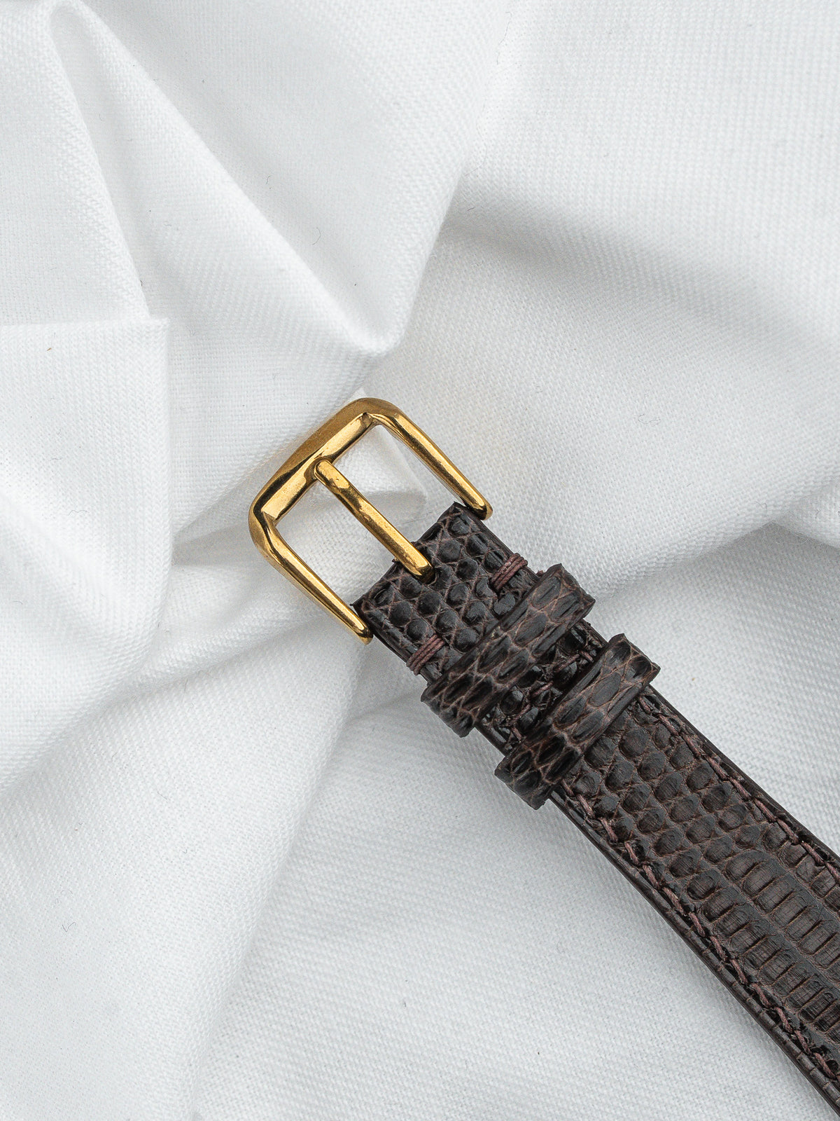 Bracelet de montre en cuir brun façon crocodile avec boucle dorée sur fond blanc