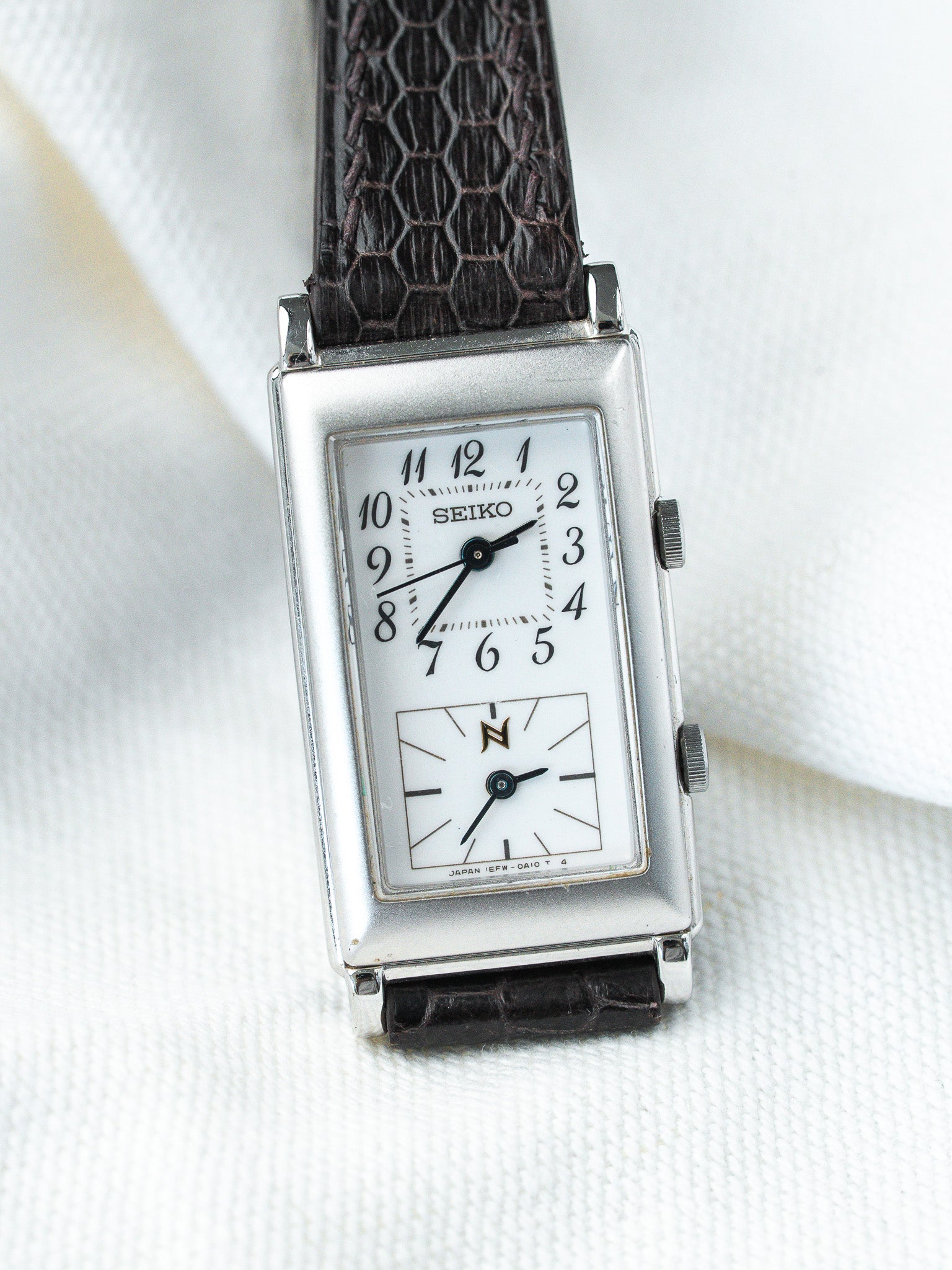 Vintage Seiko rectangular watch with white dial, black numerals, and dark textured strap