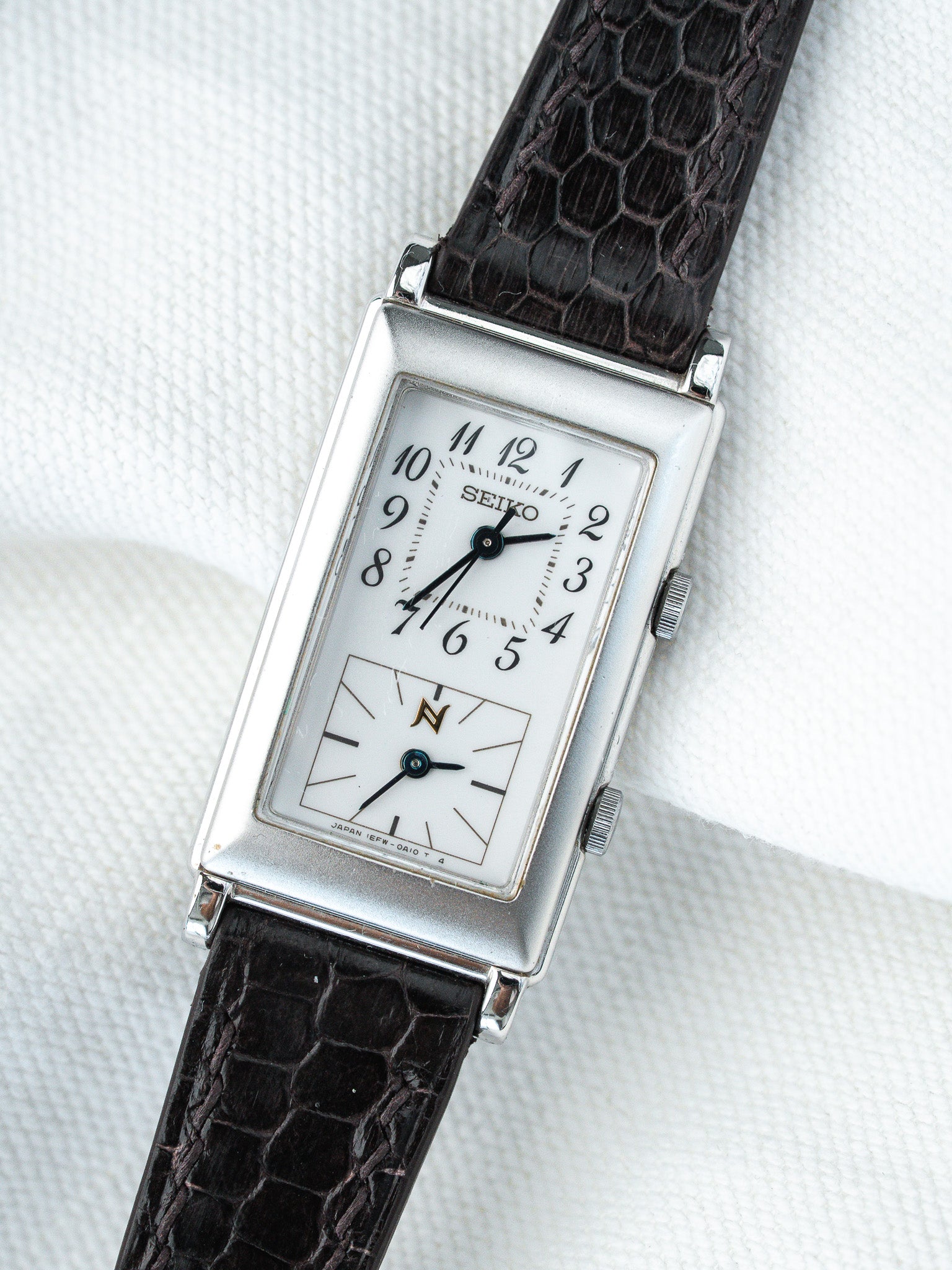 Seiko vintage rectangular watch with white dial, black leather strap, on textured white background