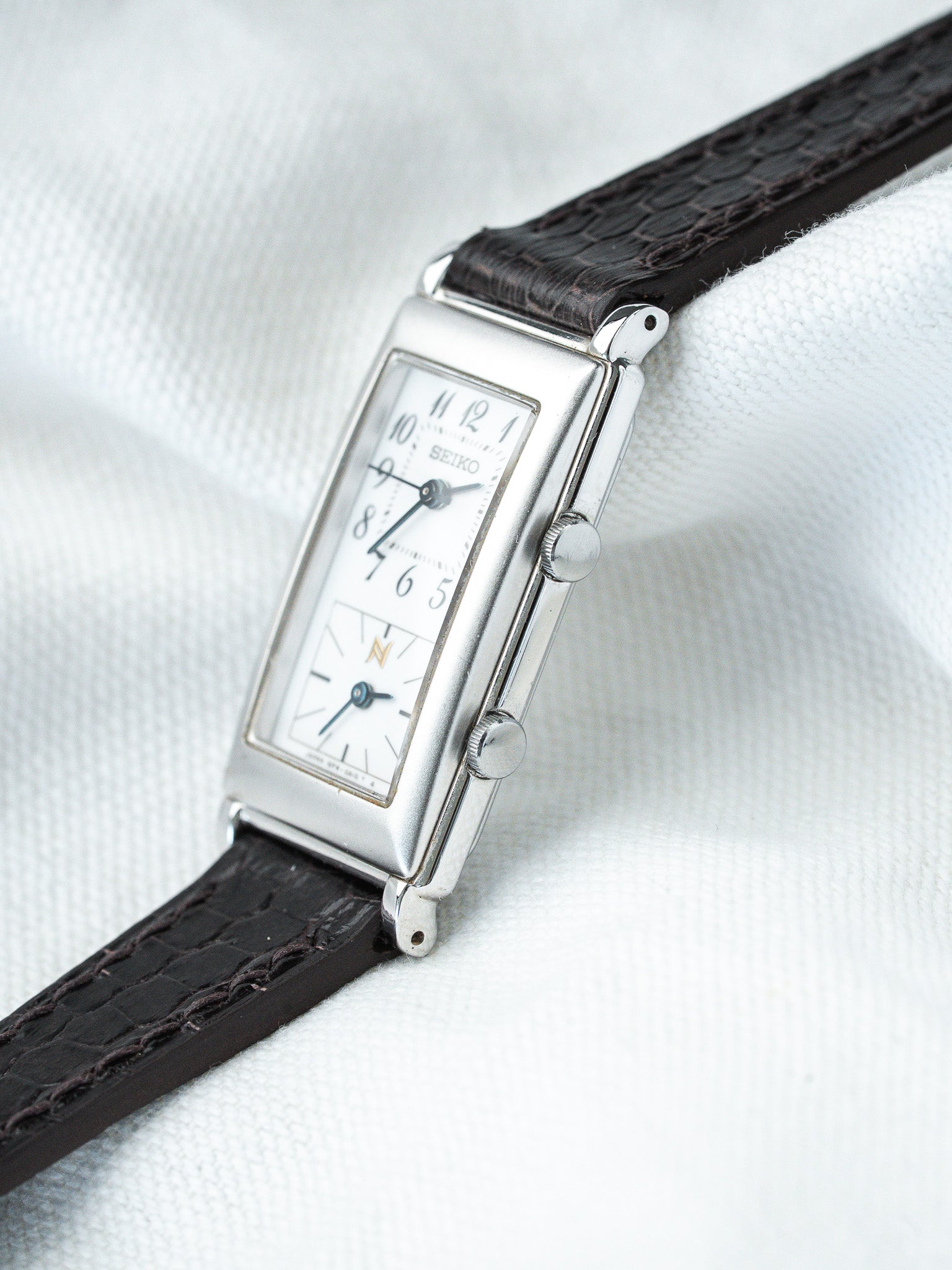 Seiko vintage watch with rectangular silver case, white dial, black alligator strap on white fabric