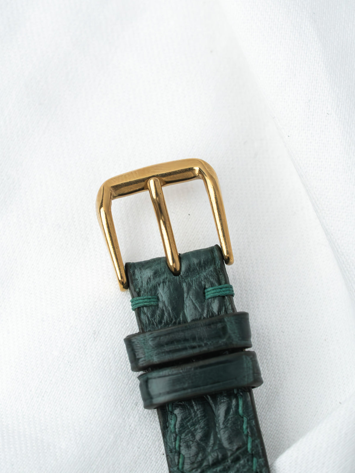 Vintage watch strap with green alligator leather and gold buckle on white background