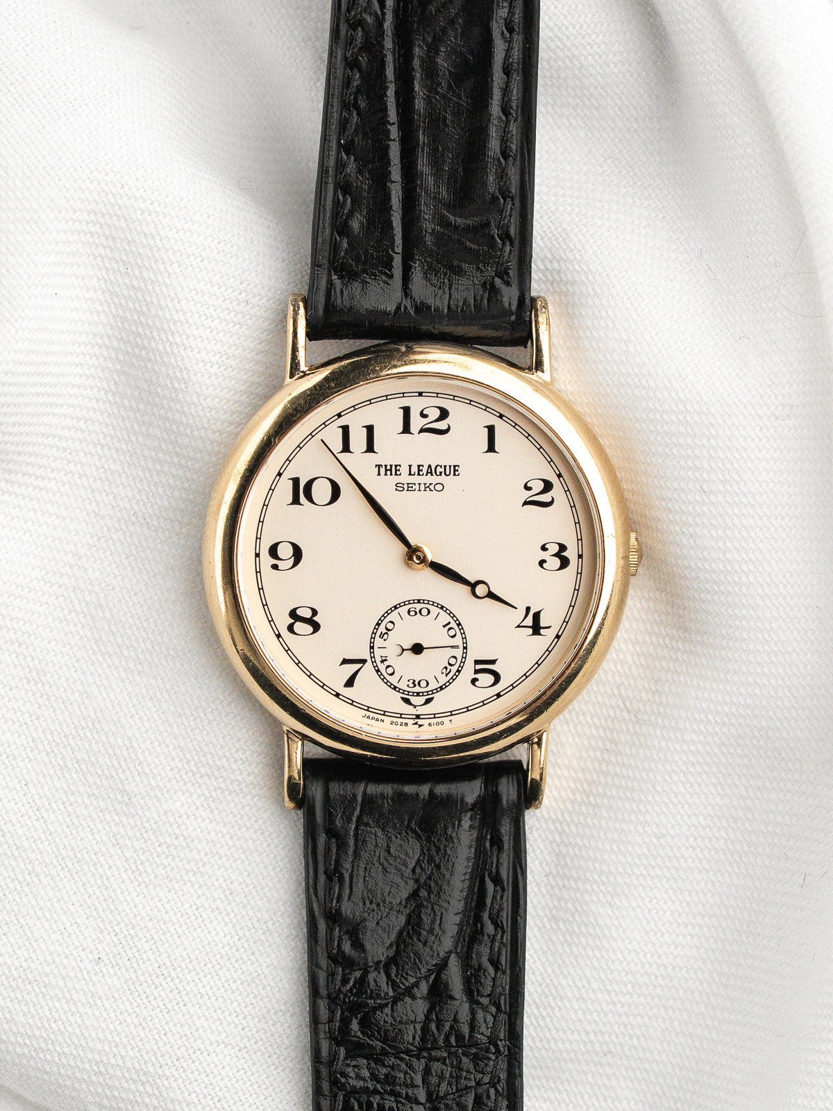 Montre Seiko The League vintage au boîtier doré et bracelet en cuir noir.