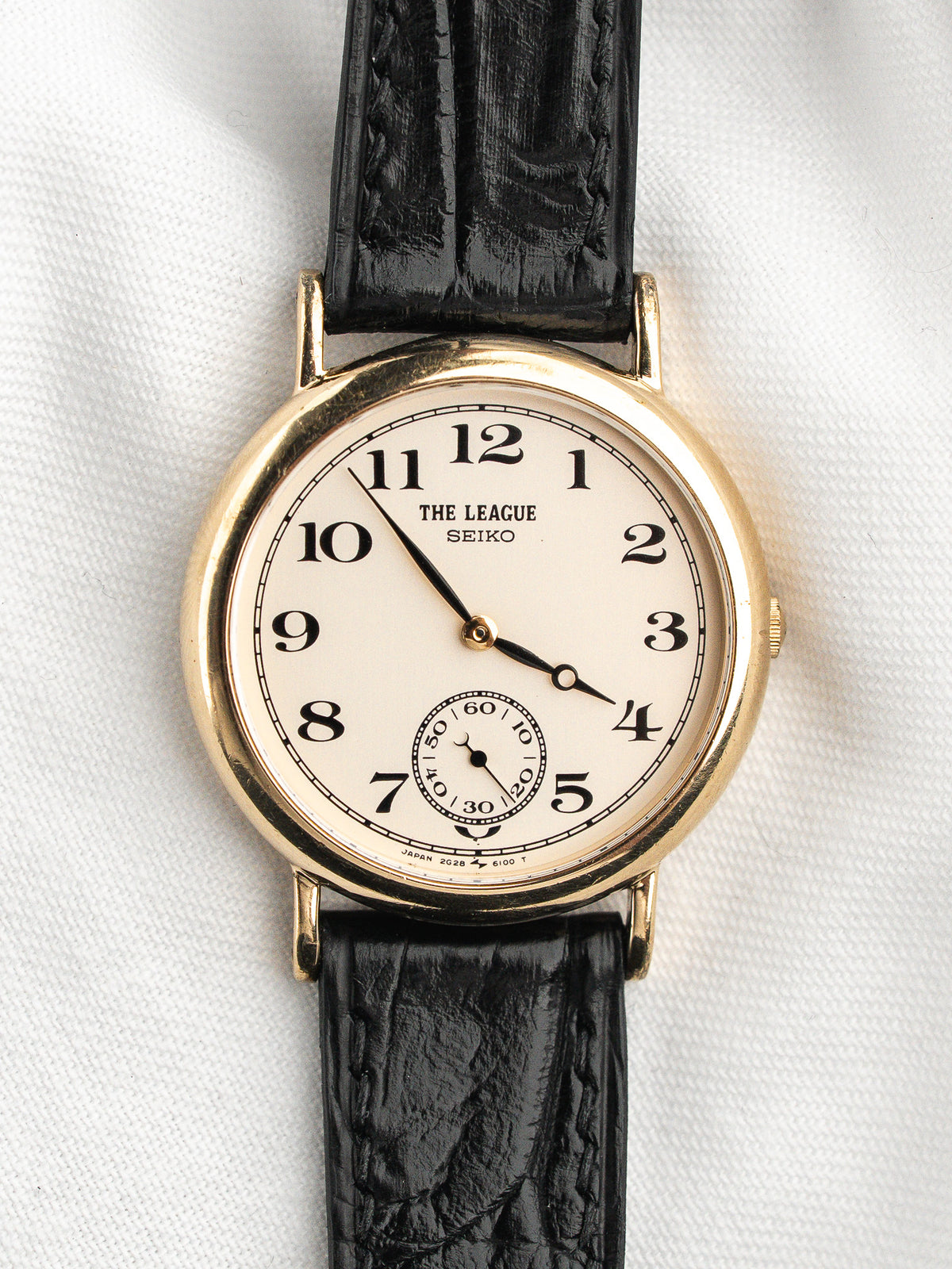 Montre vintage Seiko The League au boîtier doré avec bracelet en cuir noir.