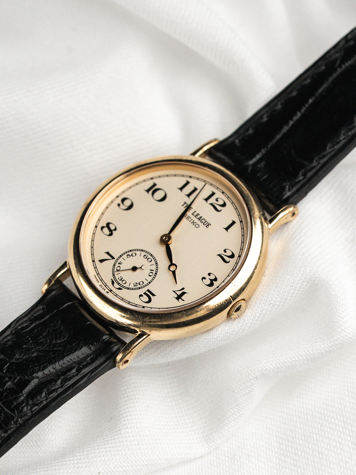 Montre vintage avec boîtier doré, cadran blanc et bracelet en cuir noir grainé.