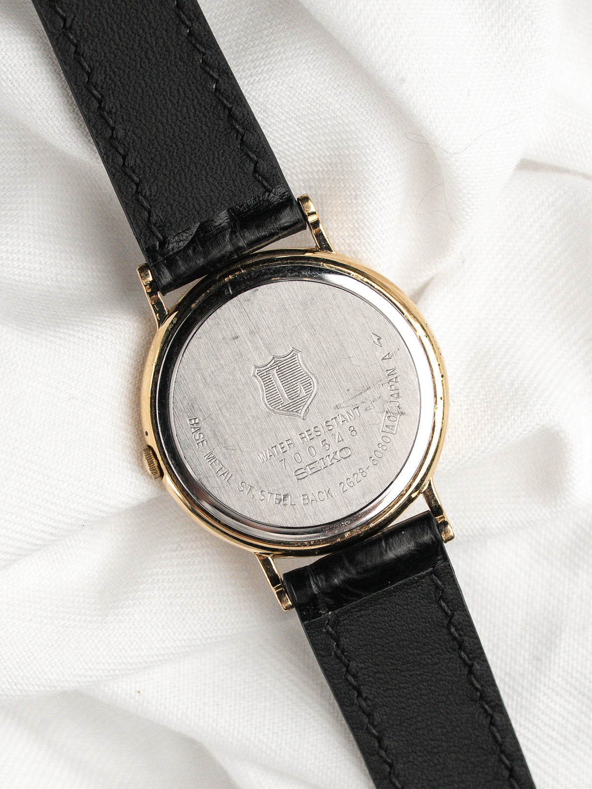 Dos d'une montre Seiko en acier et or avec bracelet en cuir noir.