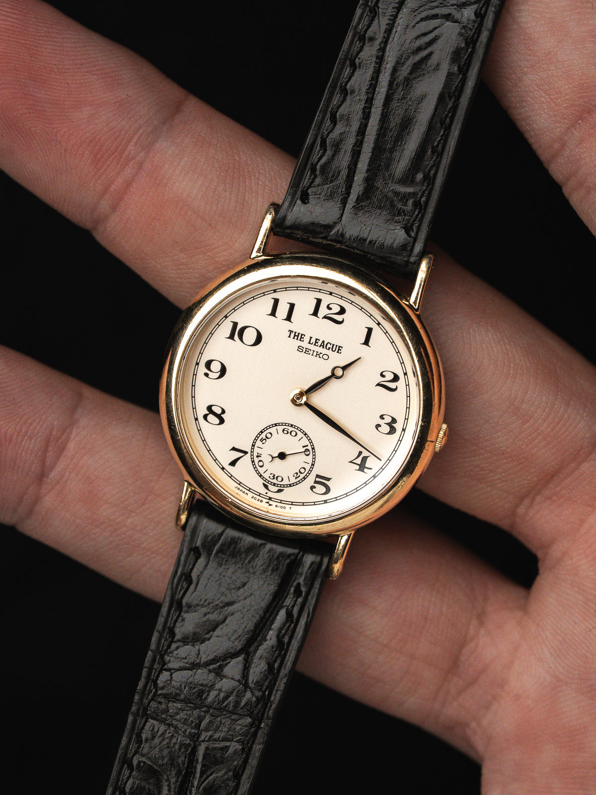 Montre vintage Seiko avec cadran blanc, boîtier doré et bracelet en cuir noir.