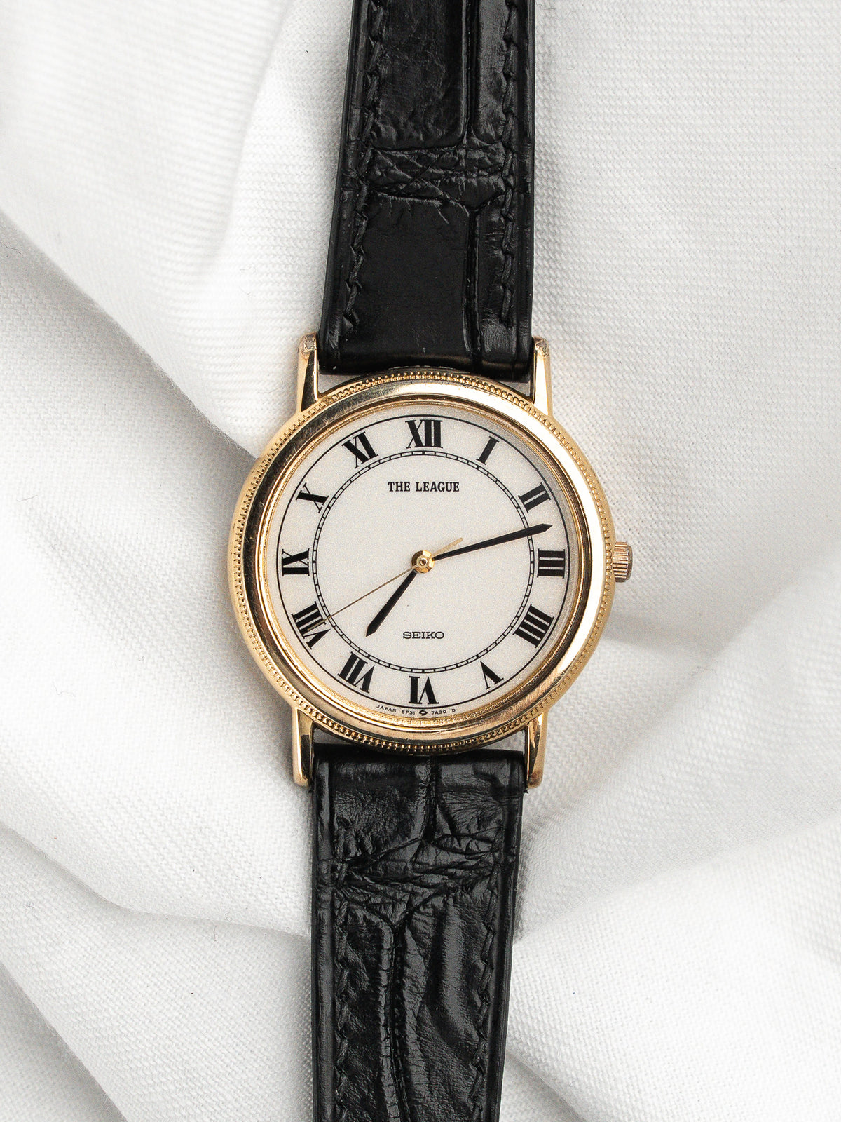Montre Seiko vintage avec cadran blanc, chiffres romains et bracelet en cuir noir.