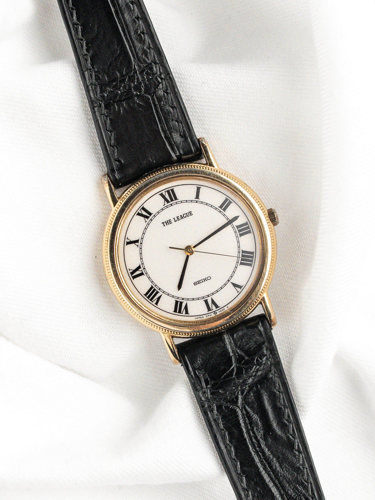 Montre Seiko The League vintage avec cadran blanc, chiffres romains et bracelet cuir noir.