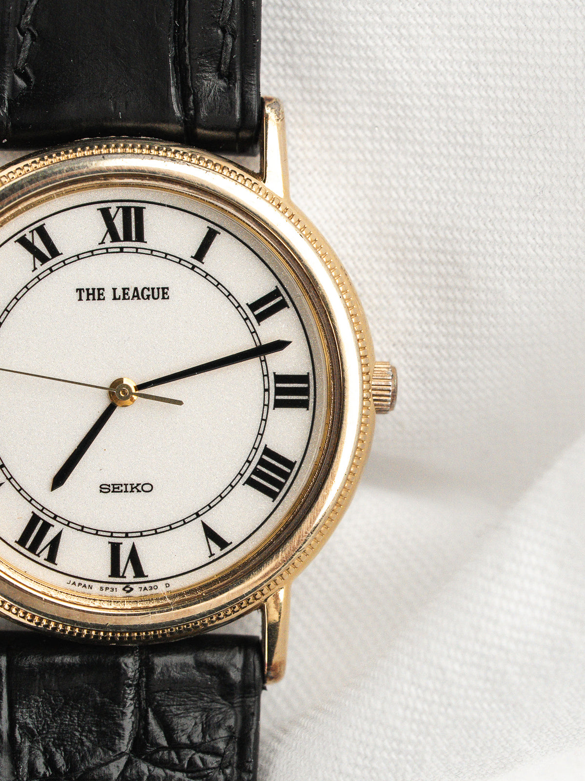Montre Seiko avec cadran blanc, chiffres romains et bracelet en cuir noir.