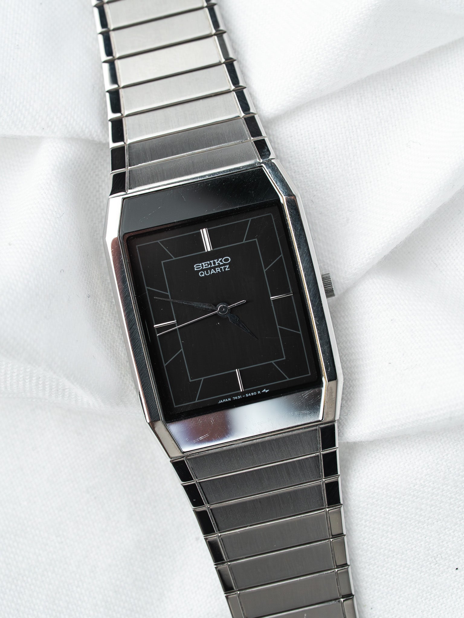 Seiko Quartz vintage watch with black dial, geometric markers, and stainless steel bracelet on white fabric