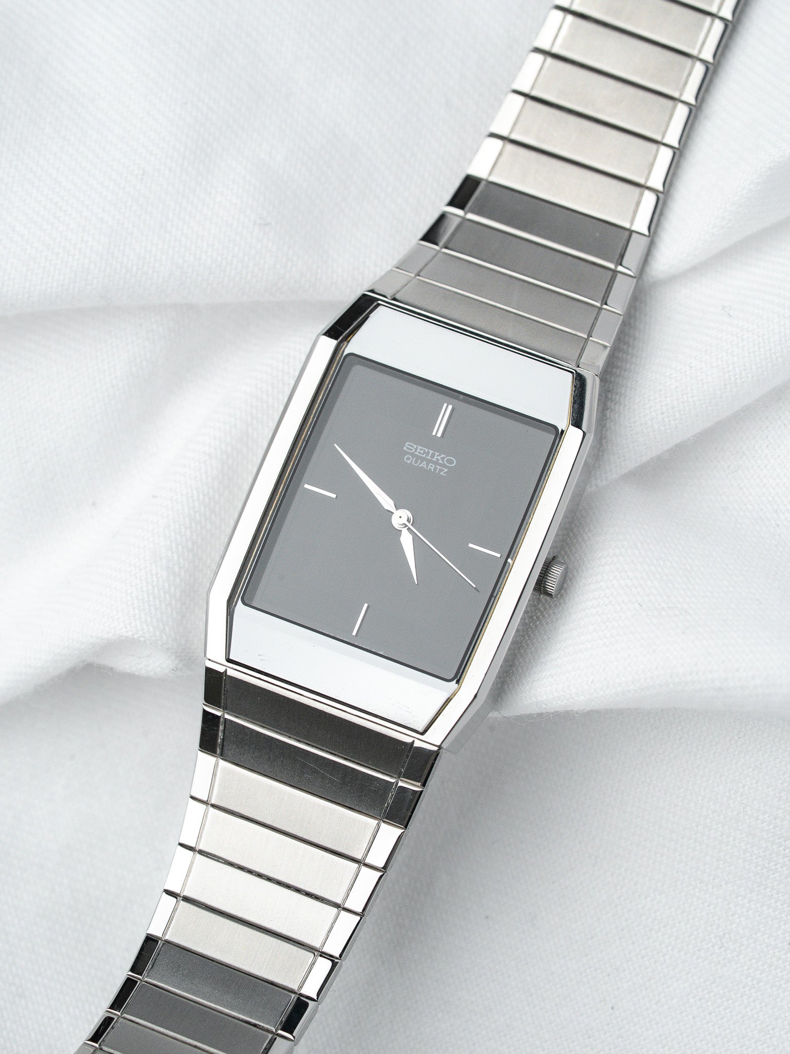 Seiko Quartz vintage watch with grey dial, silver case, and metal bracelet on white fabric