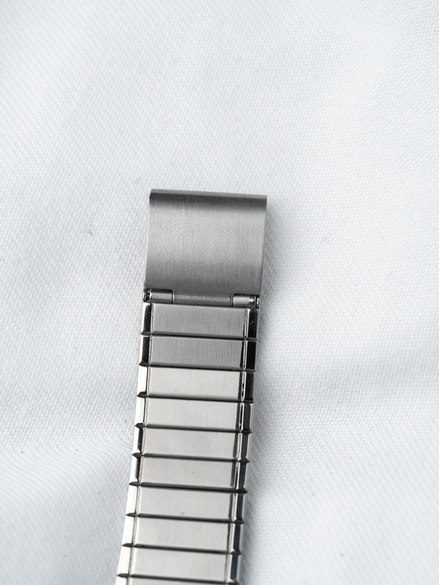 Stainless steel watch bracelet with brushed finish, laid on white fabric background