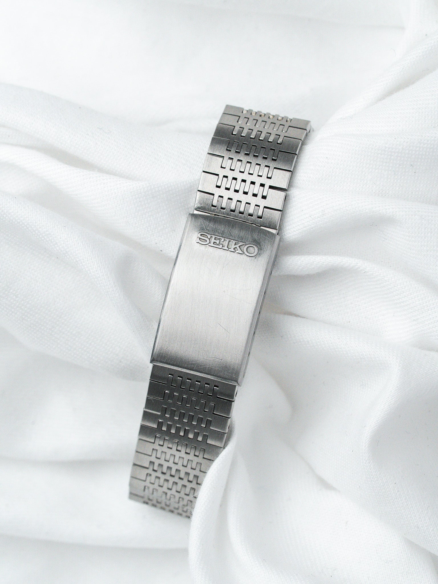Seiko vintage watch bracelet in stainless steel with textured links on white fabric