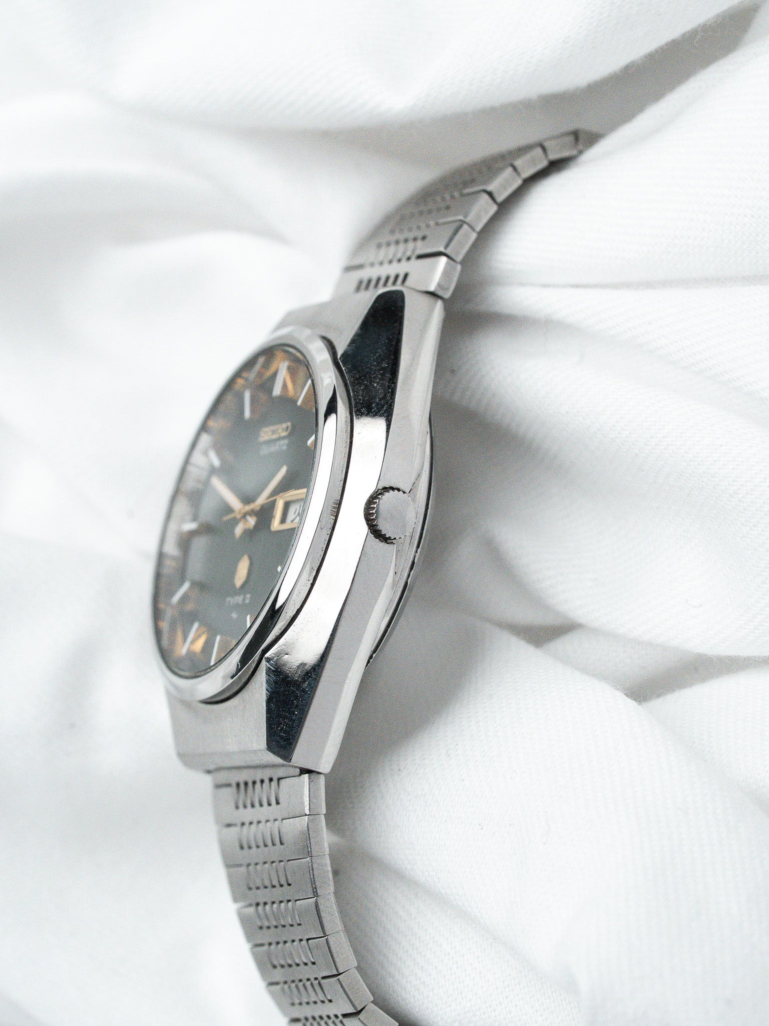Vintage Seiko Type 3 watch with dark dial, gold markers, steel bracelet on white fabric