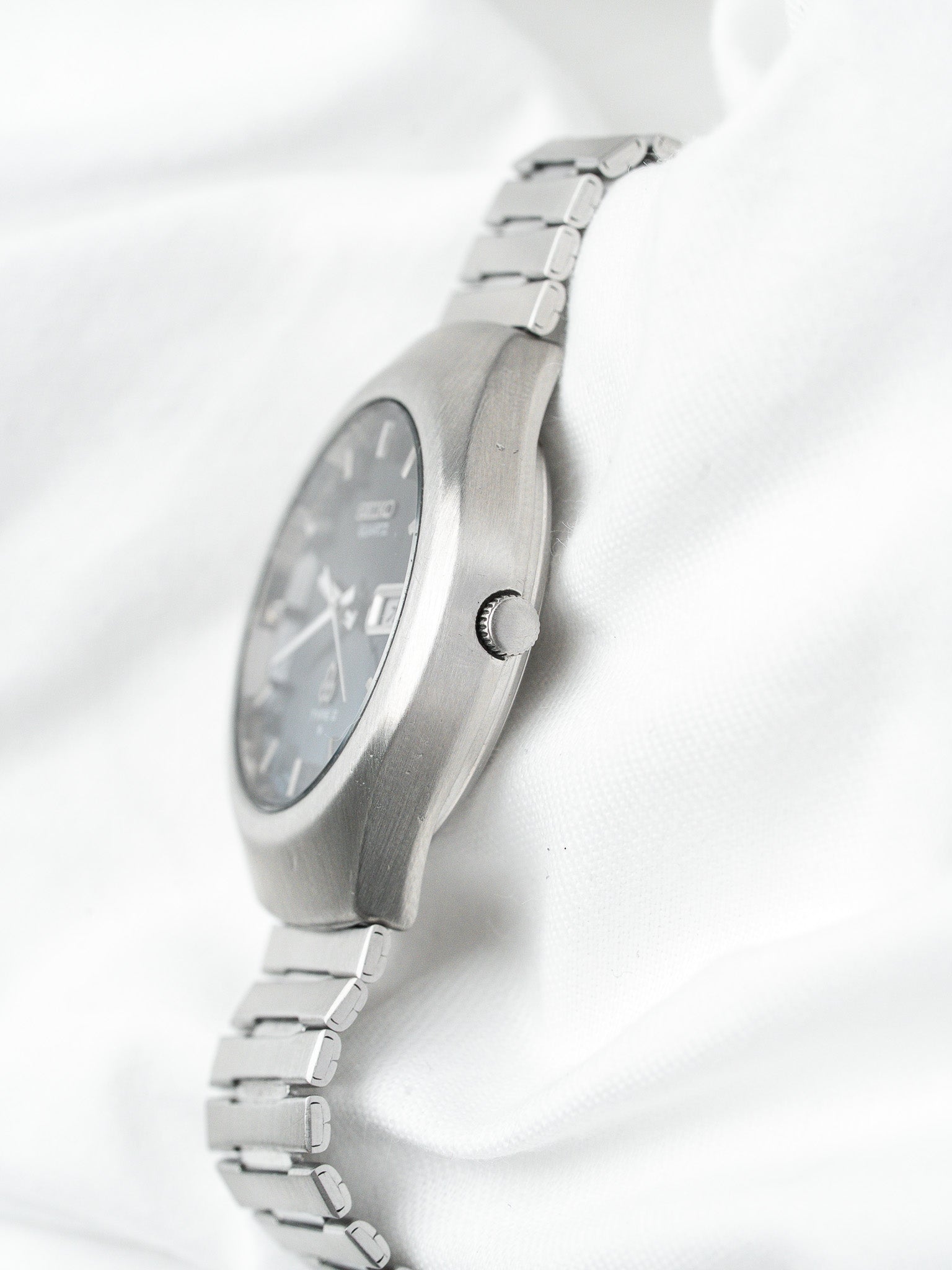Seiko vintage watch with steel case, grey dial, and metal bracelet on white fabric