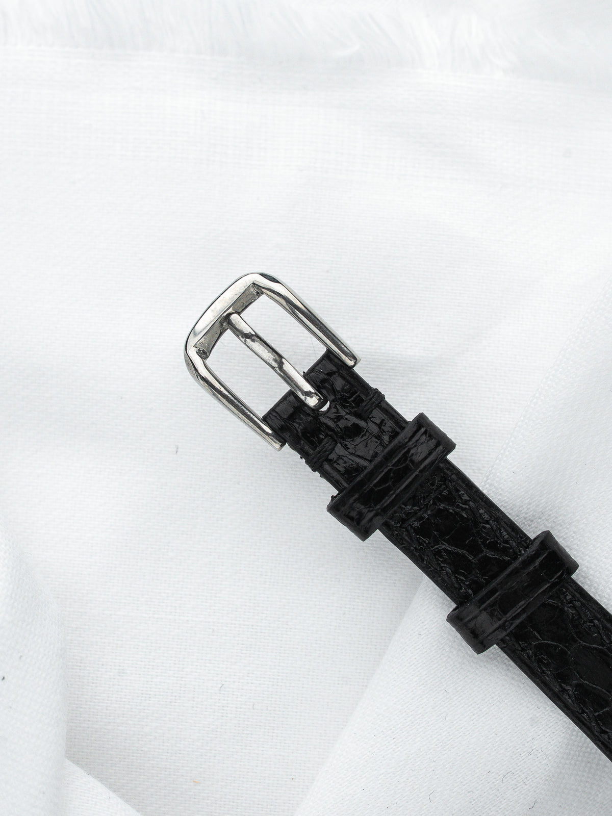 Bracelet de montre en cuir noir effet crocodile avec boucle argentée sur fond blanc