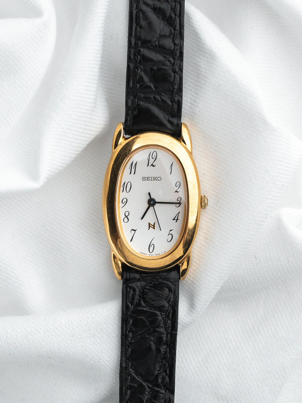 Montre Seiko vintage, boîtier ovale doré, cadran blanc et bracelet cuir noir