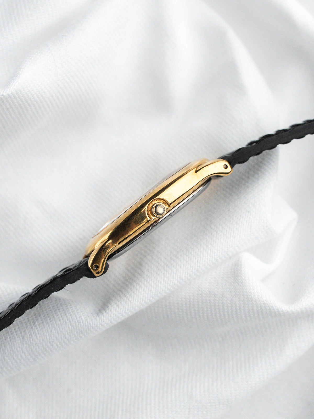 Vue de profil d'une montre vintage au boîtier doré et bracelet cuir noir