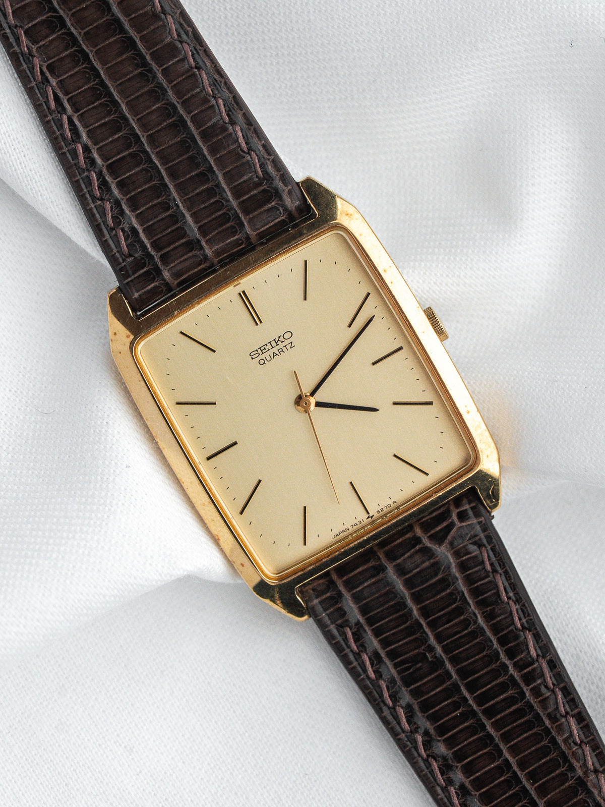 Vintage Seiko Quartz watch with gold case, cream dial, and brown lizard strap on white background